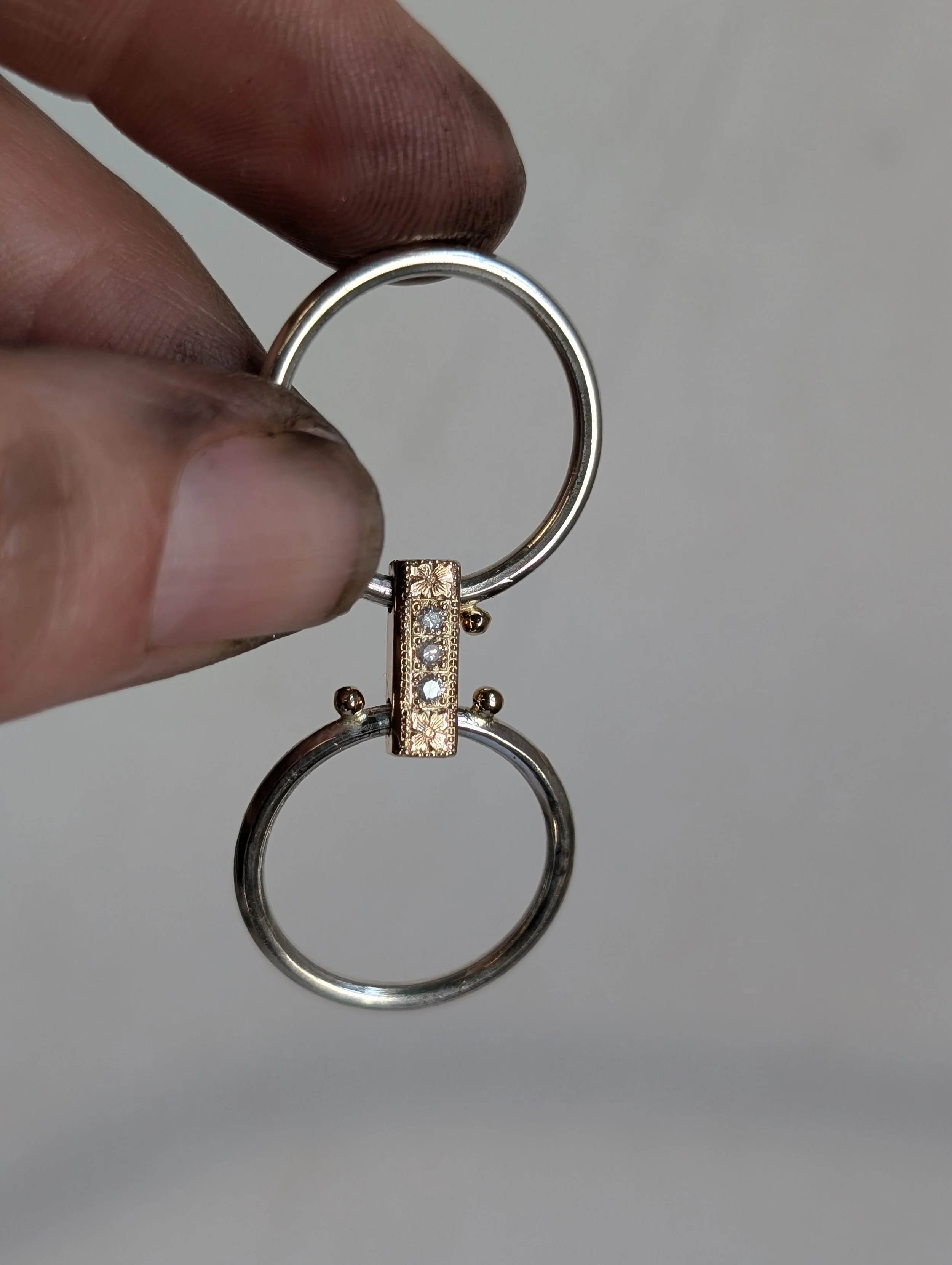 Hand holding a silver and gold keychain with a decorative rectangular bar and small clear gemstones.