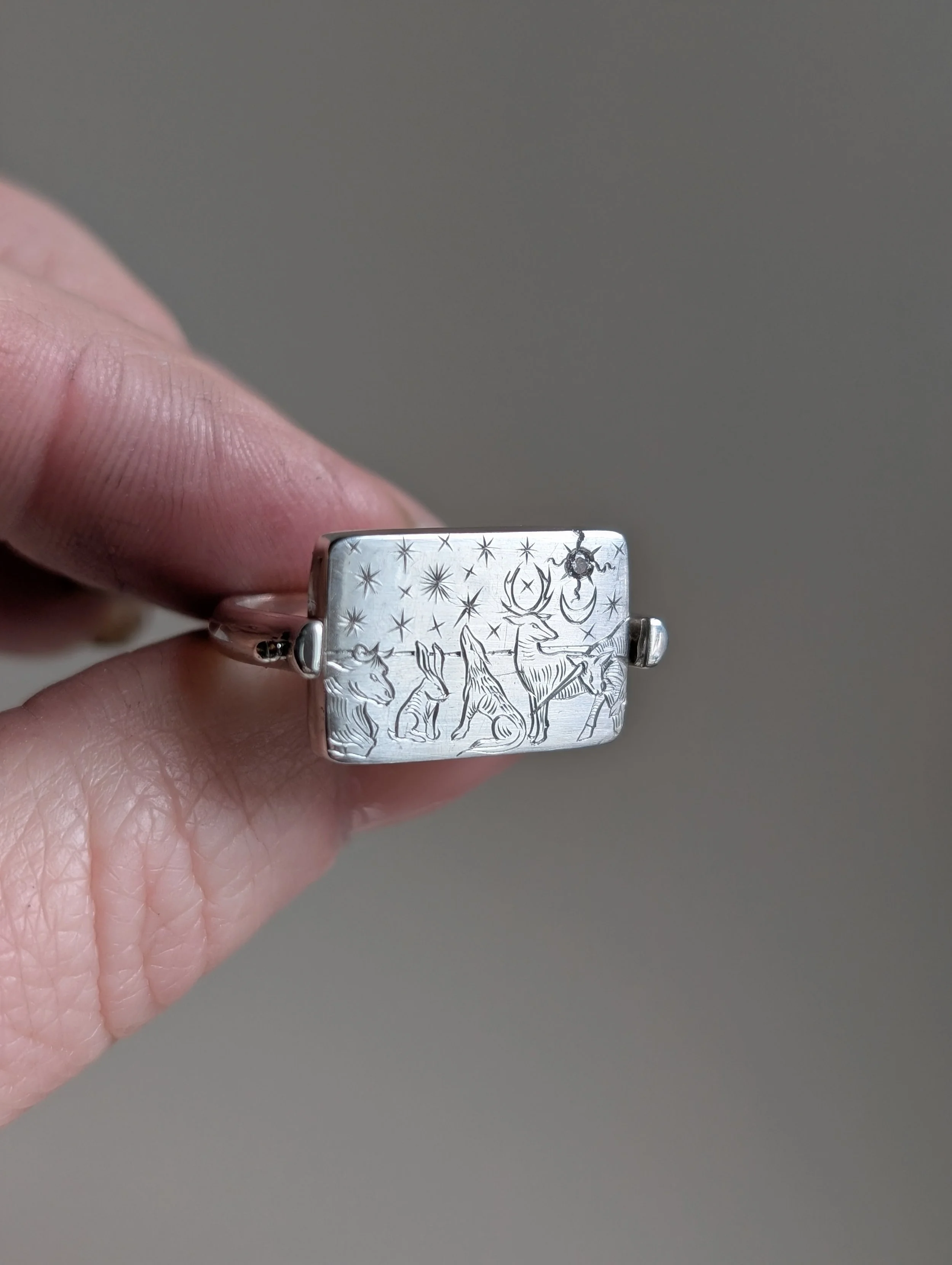 Silver ring with engraved nativity scene including animals, a deer, a rabbit, a donkey, and a cow, under stars and a moon.
