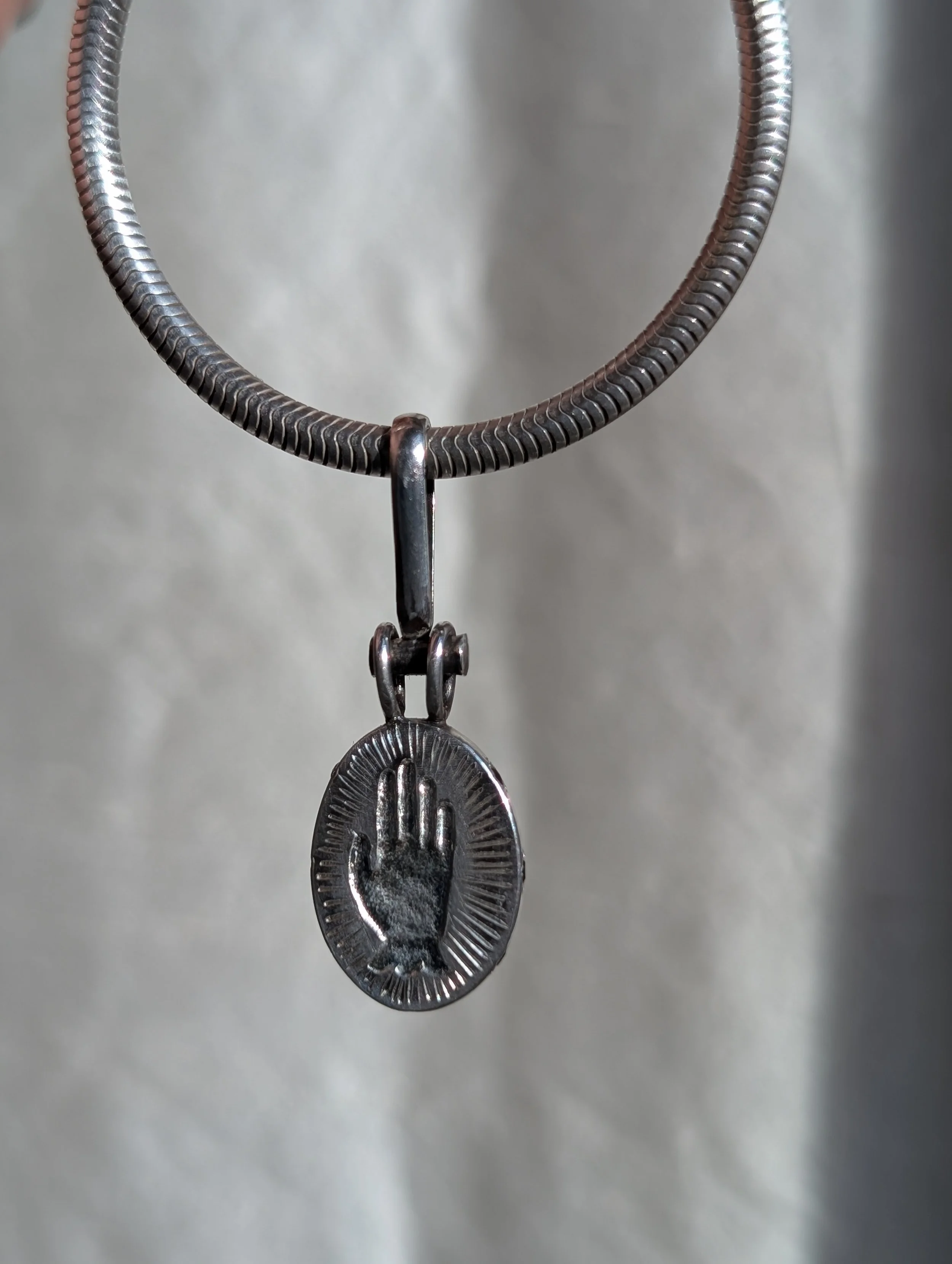 Metal necklace with a pendant featuring an engraved hand symbol