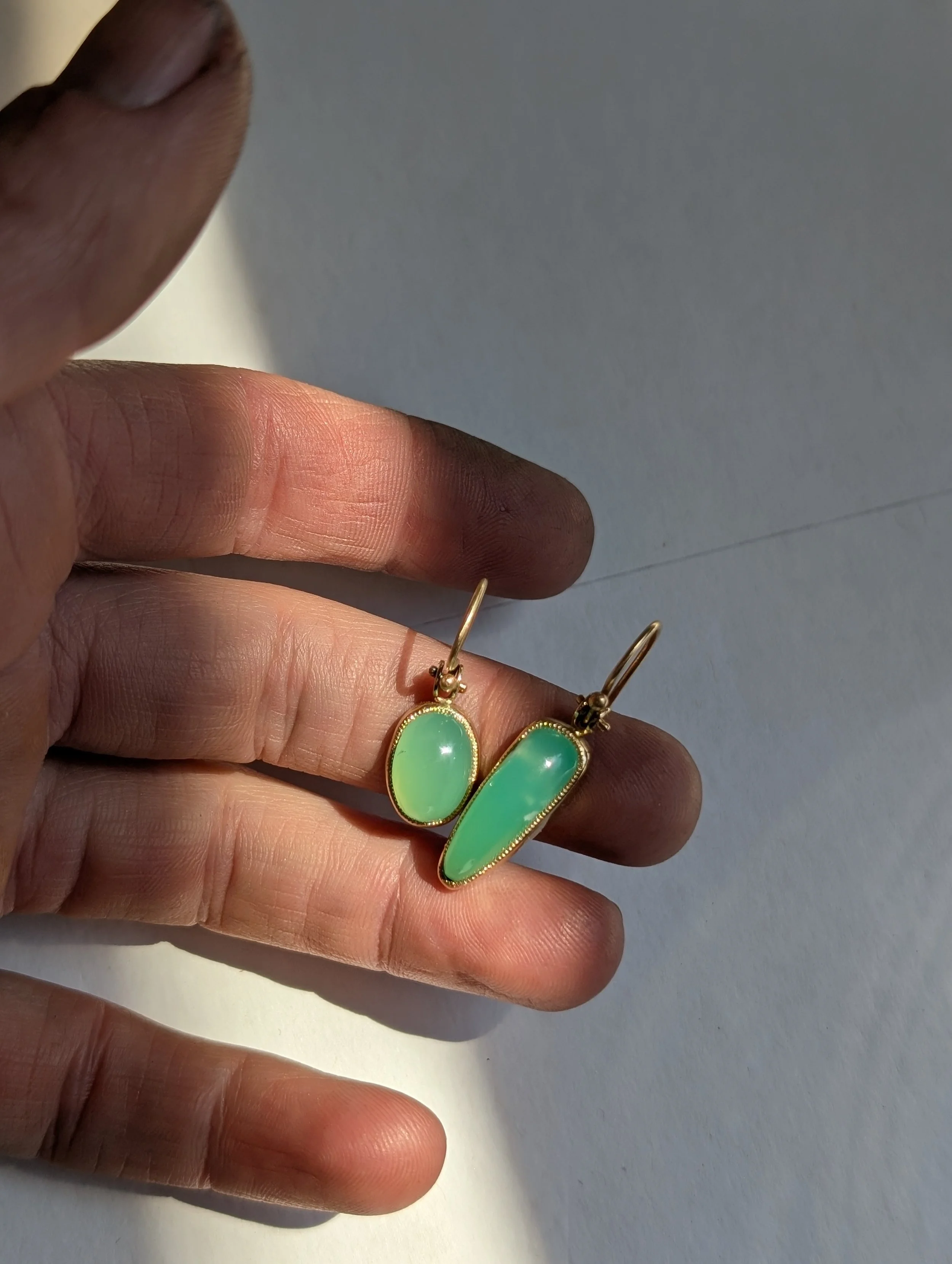 Hand holding gold earrings with green opal stones against a white background.