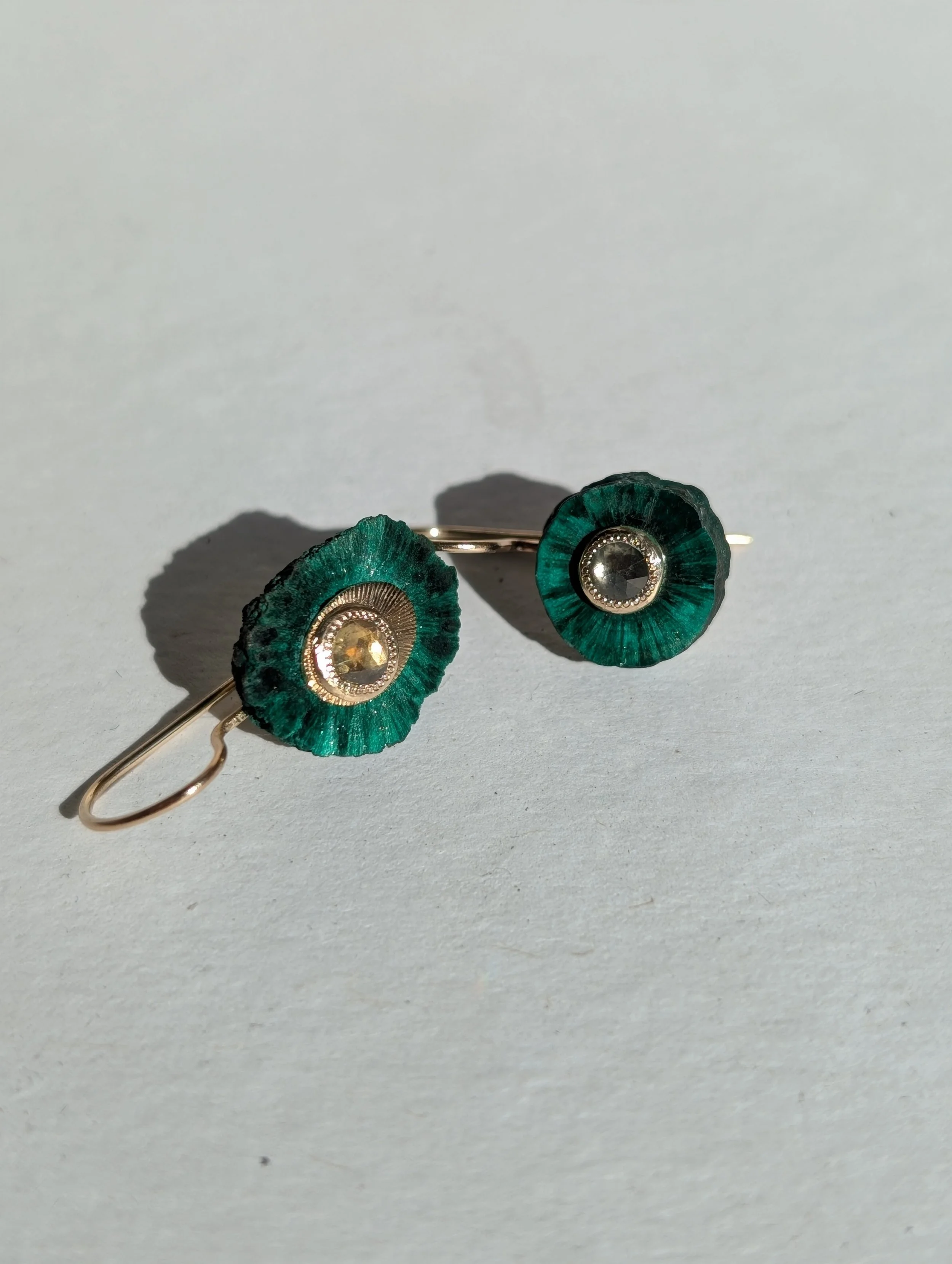 Pair of earrings with green circular flower-like design and a central gemstone, lying on a white surface.
