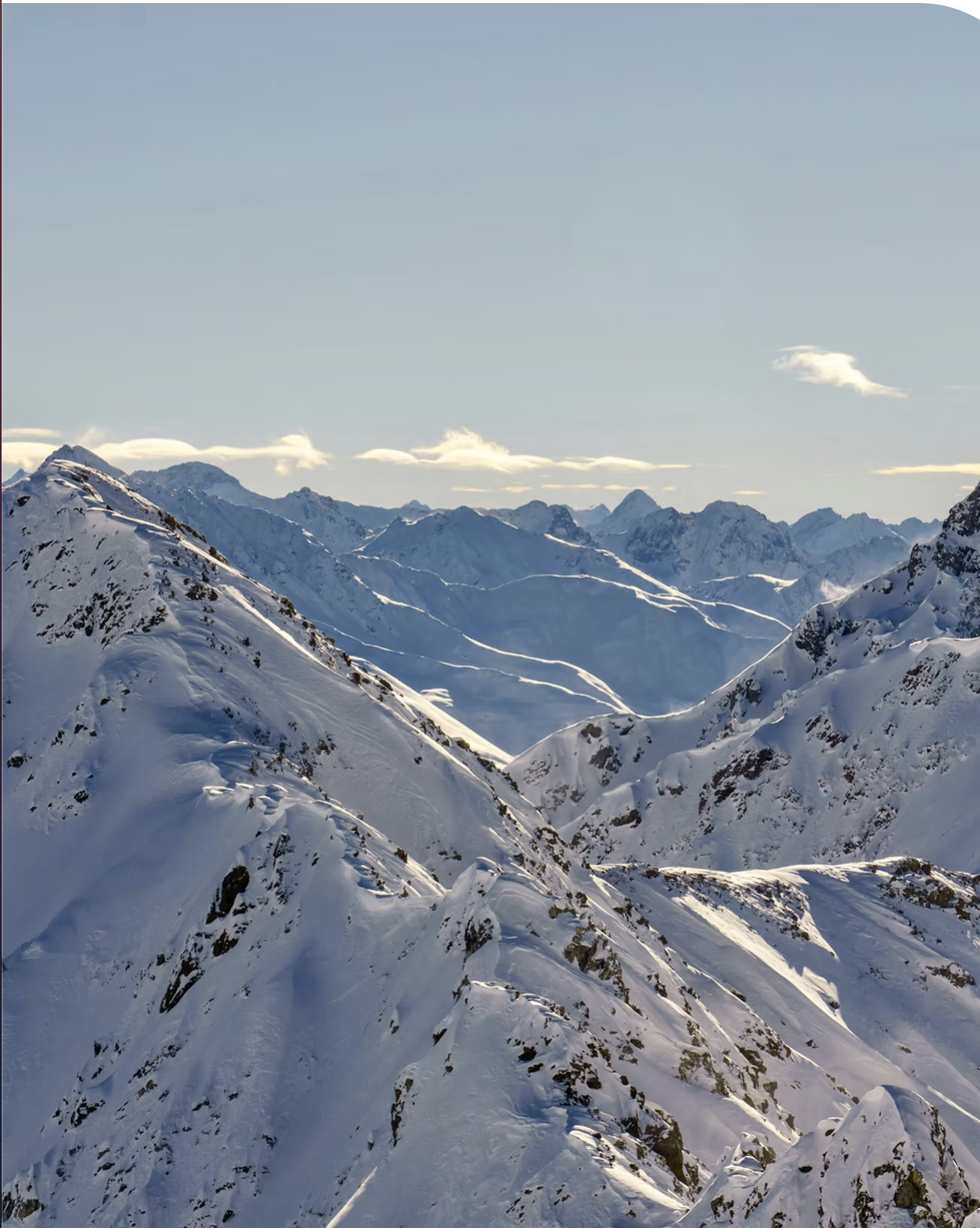 Snow-covered mountain range under a clear blue sky with some clouds.
