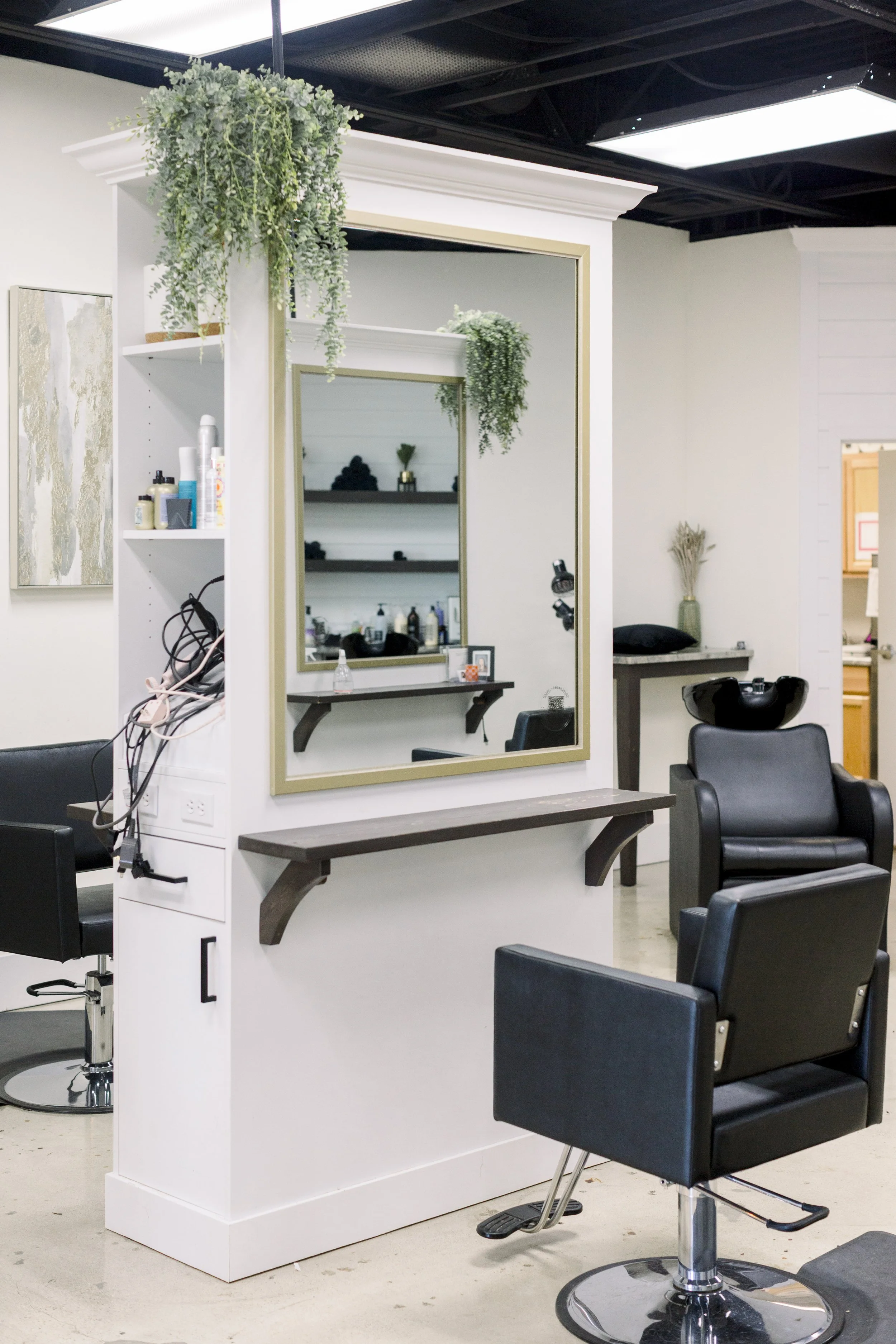 Interior view of a hair salon with styling chairs, a mirror, and shelves with hair products.