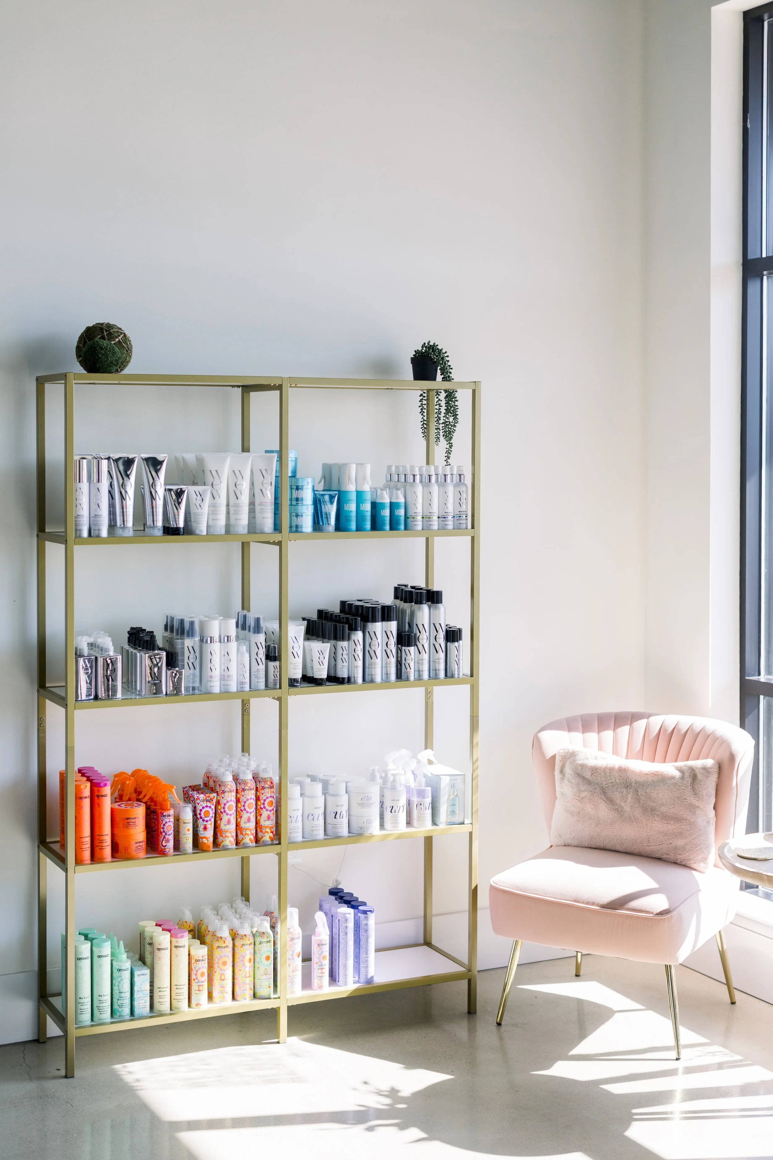 Shelves of assorted skincare products beside a pink armchair in a bright room.