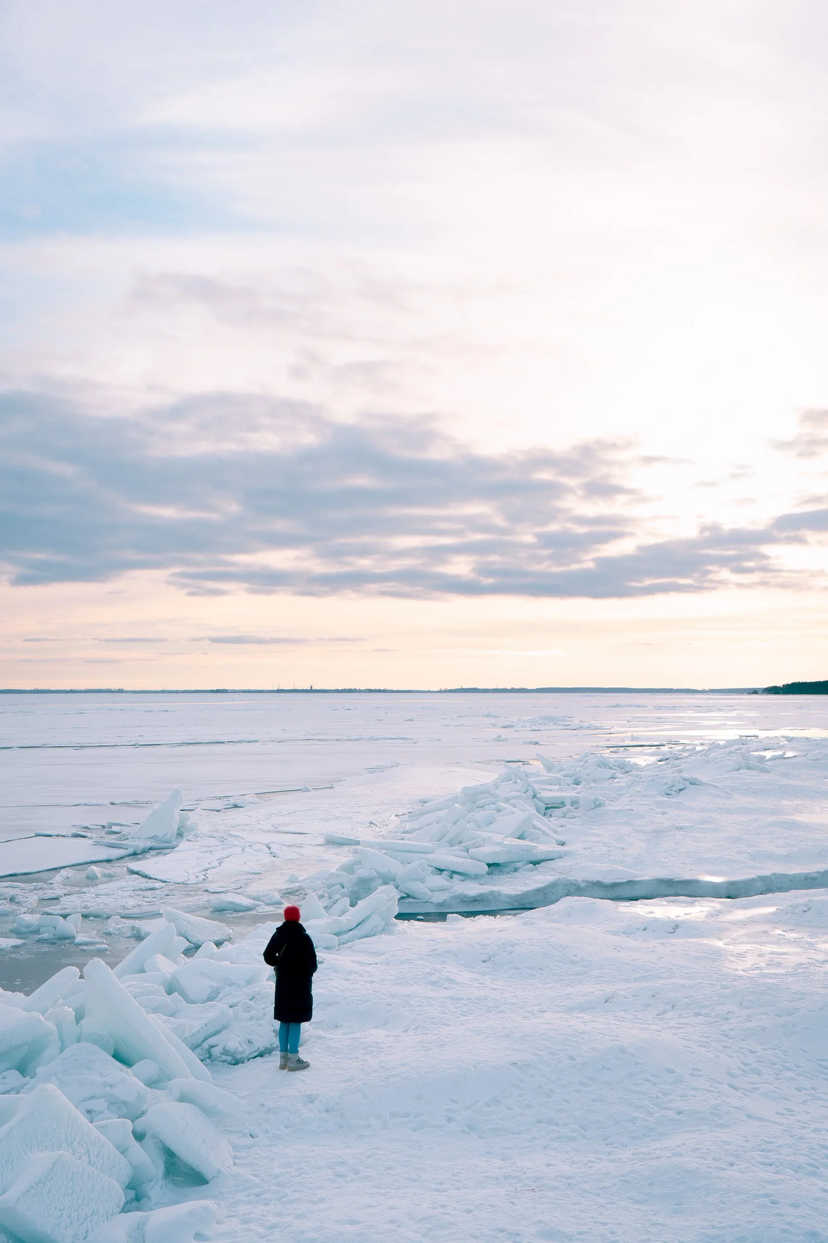 Eine Person steht auf einer gefrorenen, vereisten Landschaft mit großen Eisschollen, unter einem Himmel mit Wolken und Sonnenlicht.