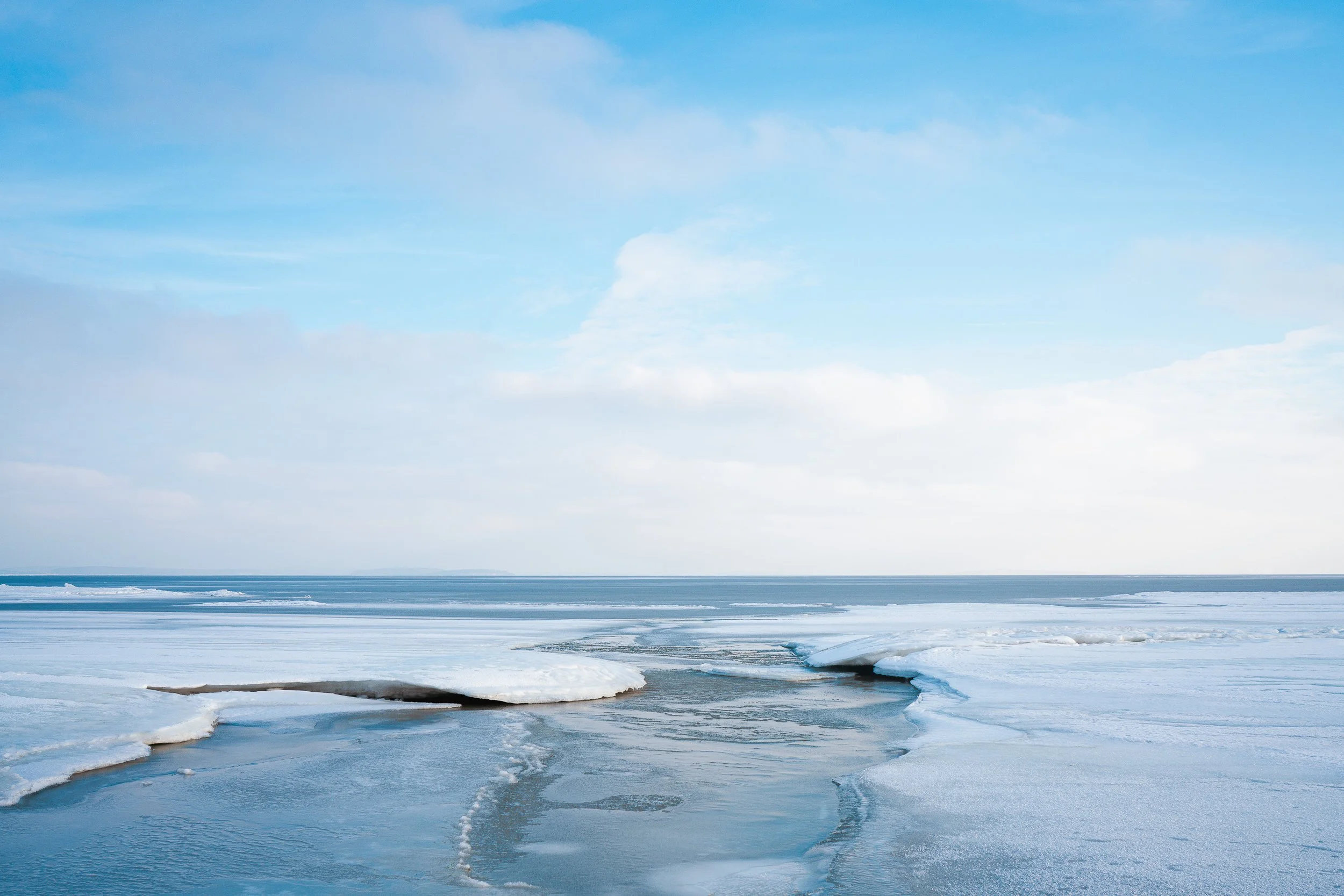 Eisiges Meer mit schmelzenden Eisschollen und einer ruhigen Wasserfläche unter einem bewölkten Himmel