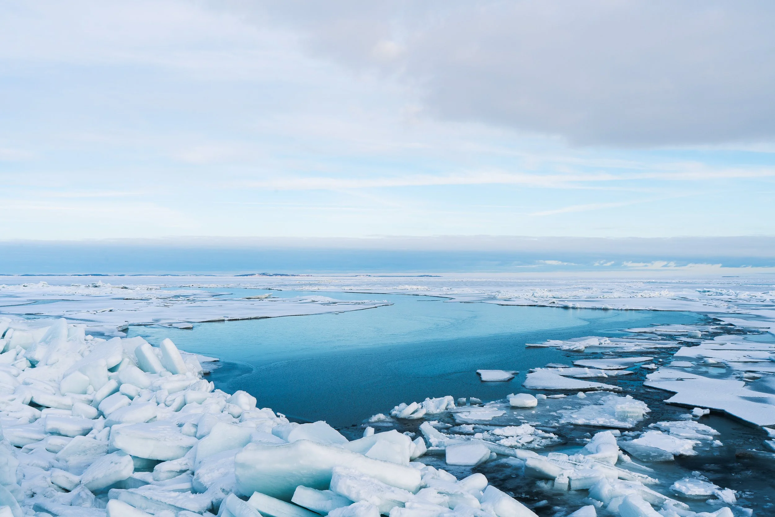 Eisiges arktisches Meeresufer mit Eisstücken am Ufer und offenem Wasser unter einem bewölkten Himmel.