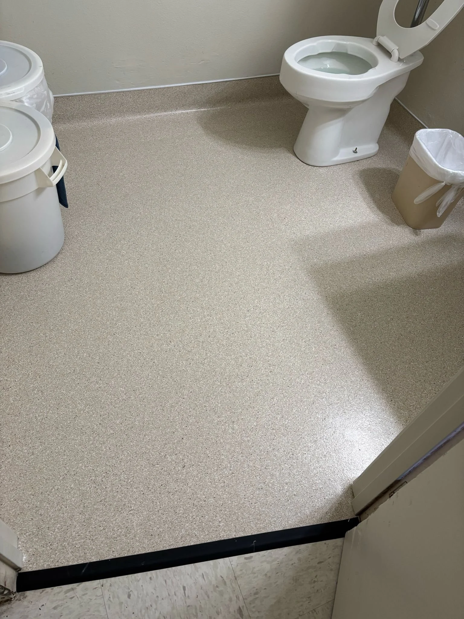 Clean restroom with a toilet, trash bin, and cleaning buckets.