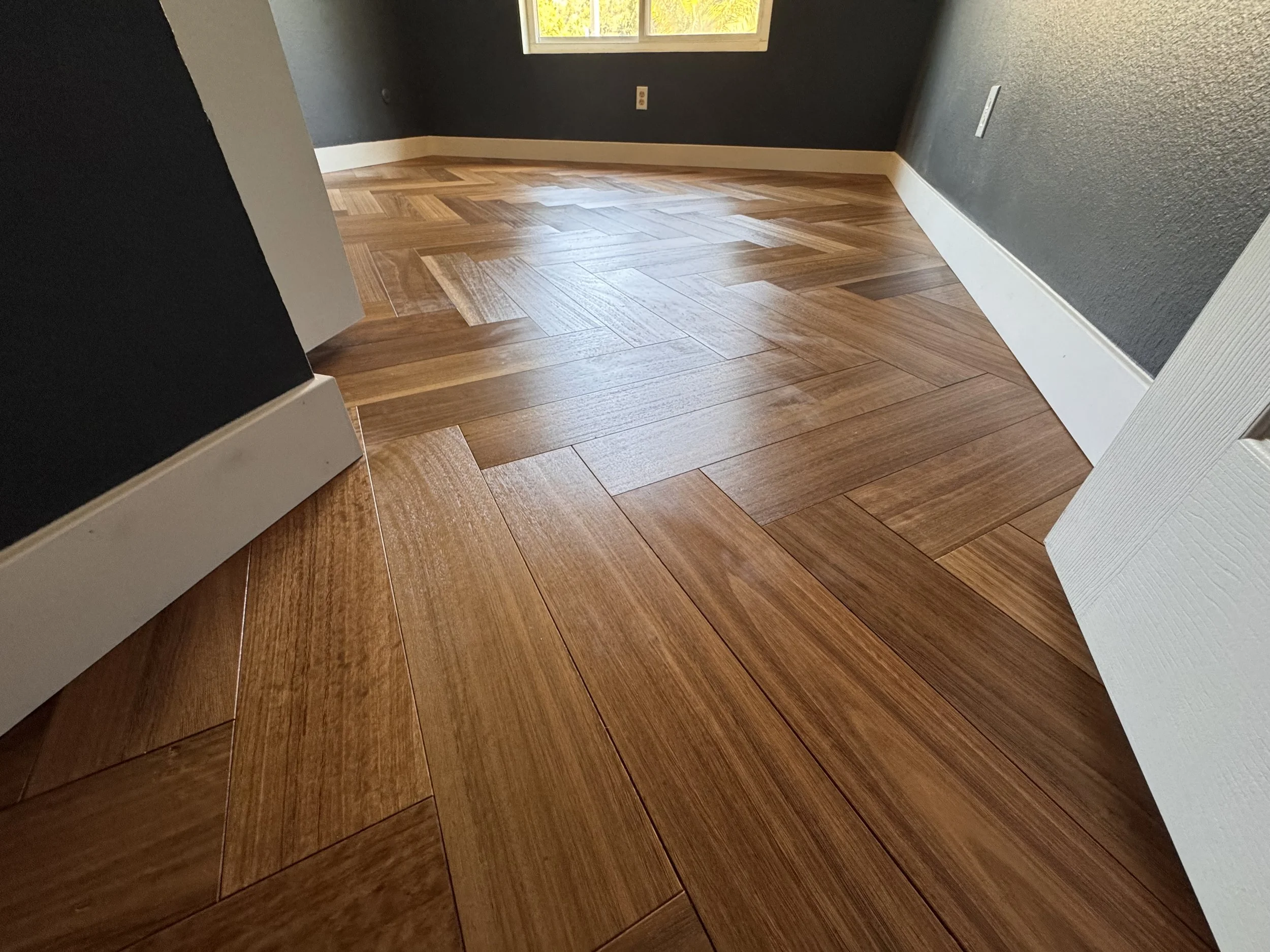 Room with hardwood floor, blue walls, a window, and white baseboards.