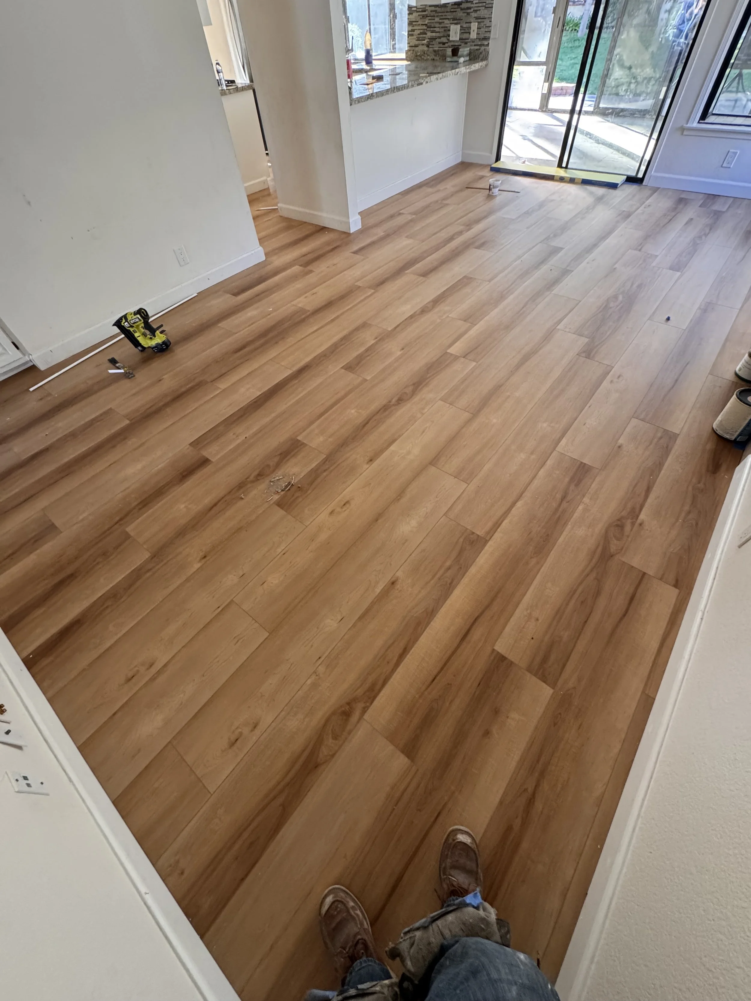 Interior view of a room with new hardwood flooring, construction tools on the floor, and a sliding glass door leading outside.