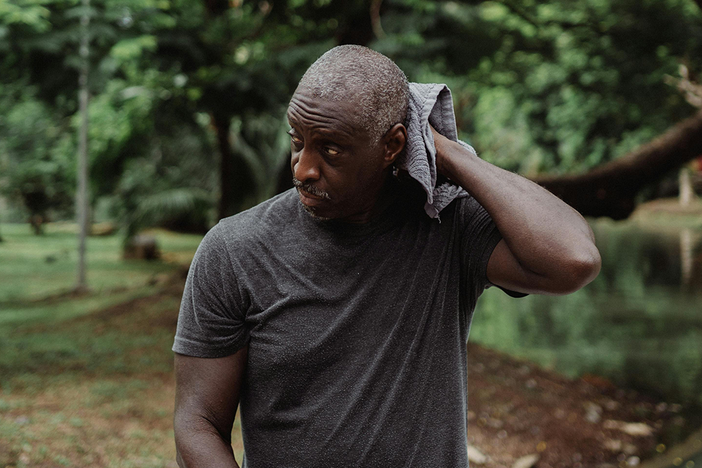 Man in a park, wiping the sweat from the back of his neck with a towel