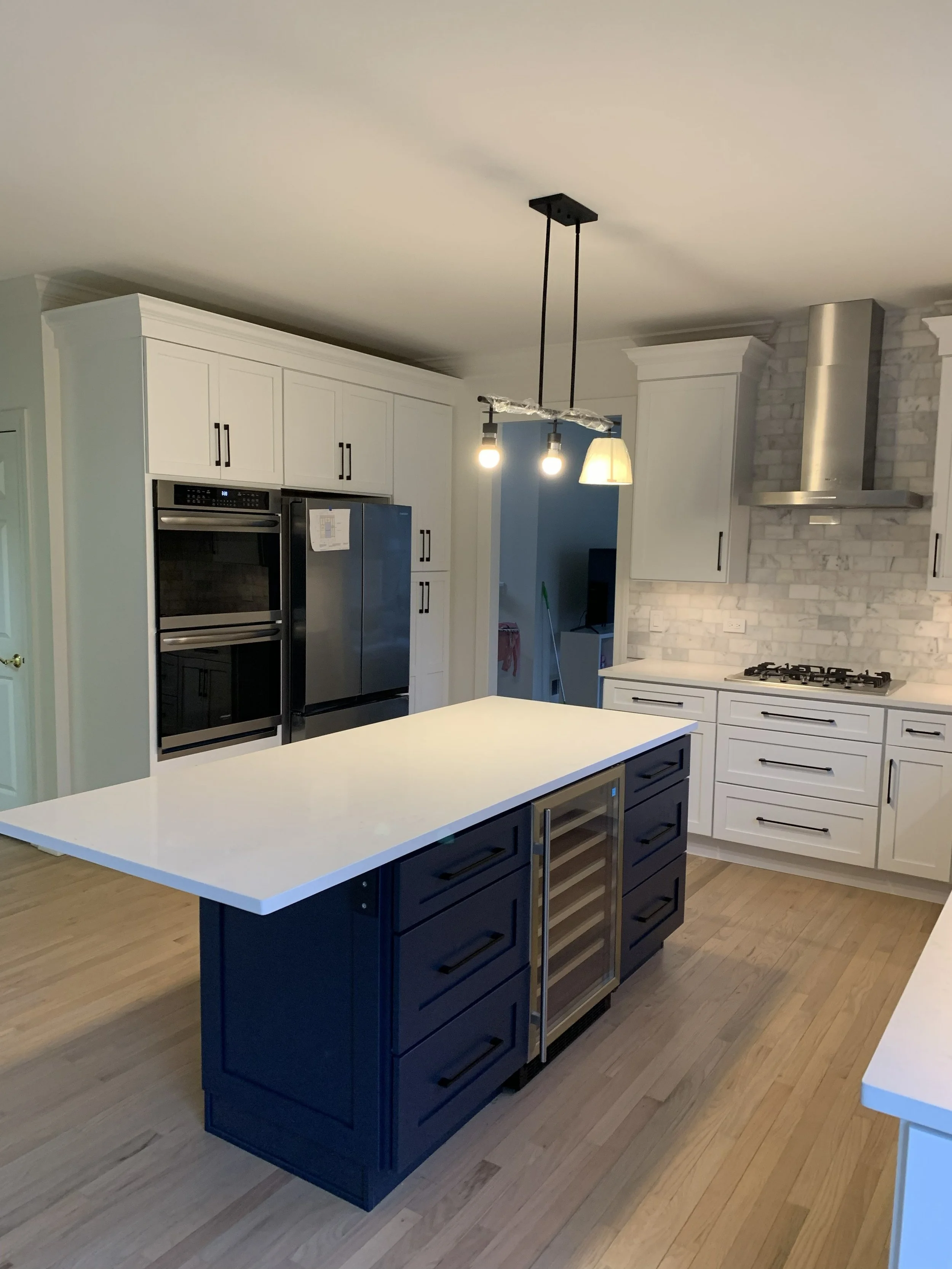 Modern kitchen with white cabinetry, stainless steel appliances, a white marble backsplash, and a central black island with a built-in wine cooler. There is a pendant light fixture hanging above the island. After pic from a remodel
