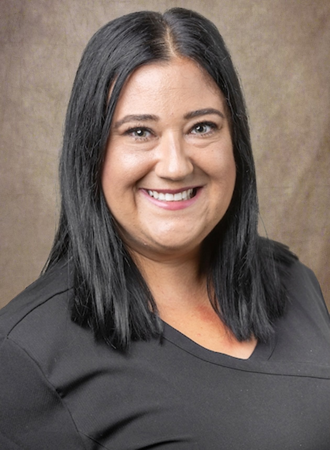Portrait of a smiling woman with black hair and a black shirt against a neutral background.