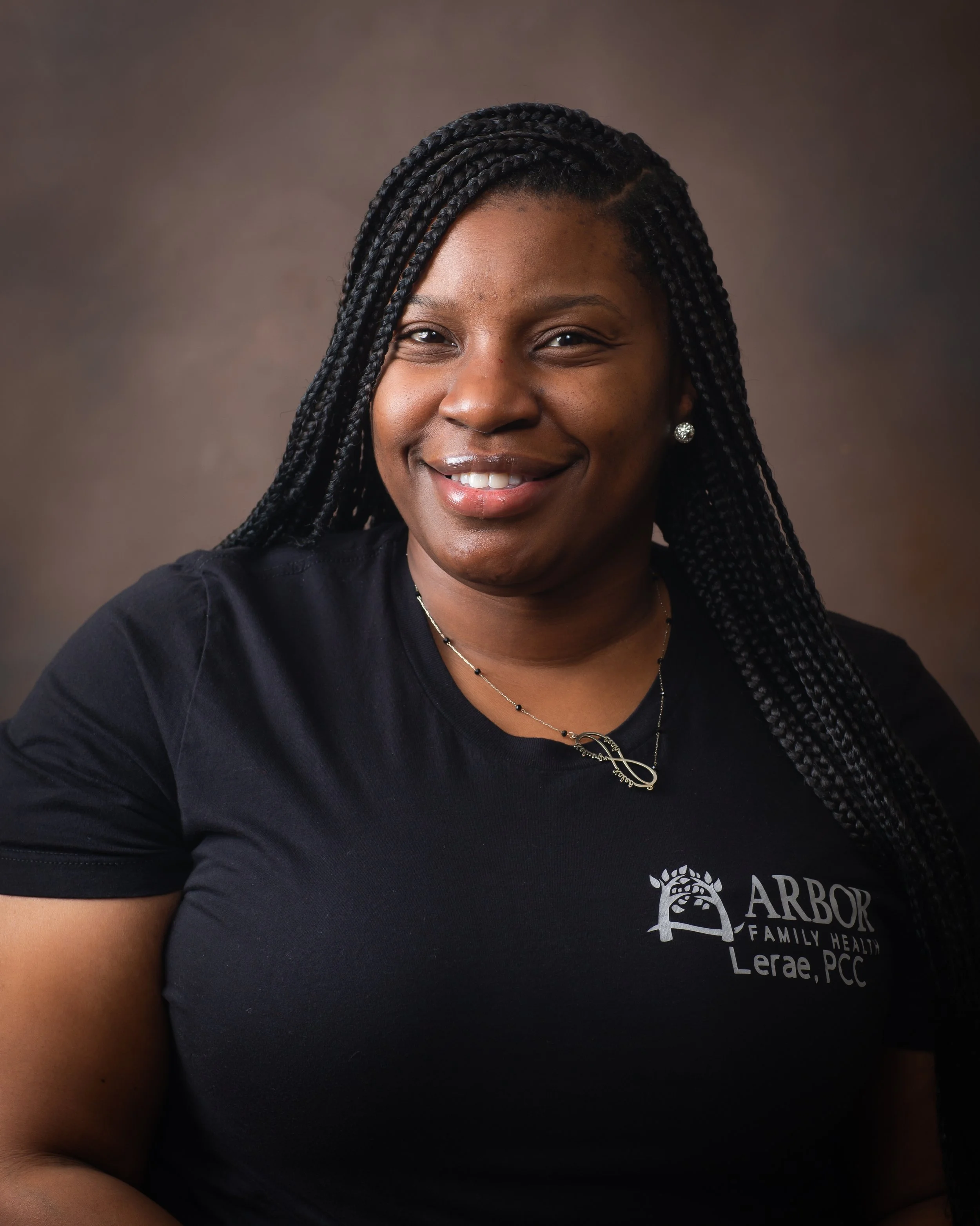 Portrait of a smiling person with braided hair wearing a black Arbor Family Health shirt.