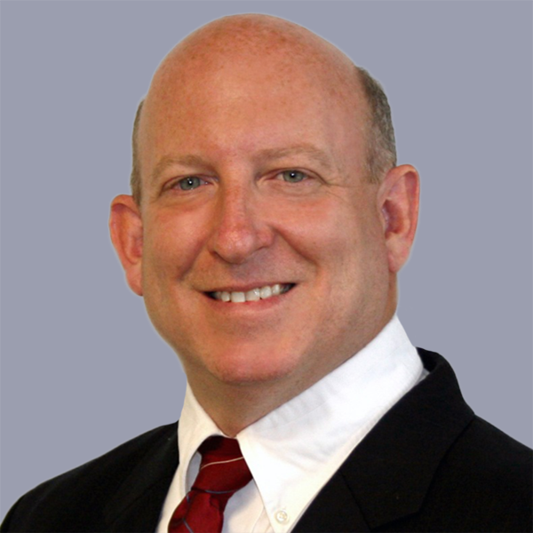 Bald man smiling in suit and tie with light gray background.