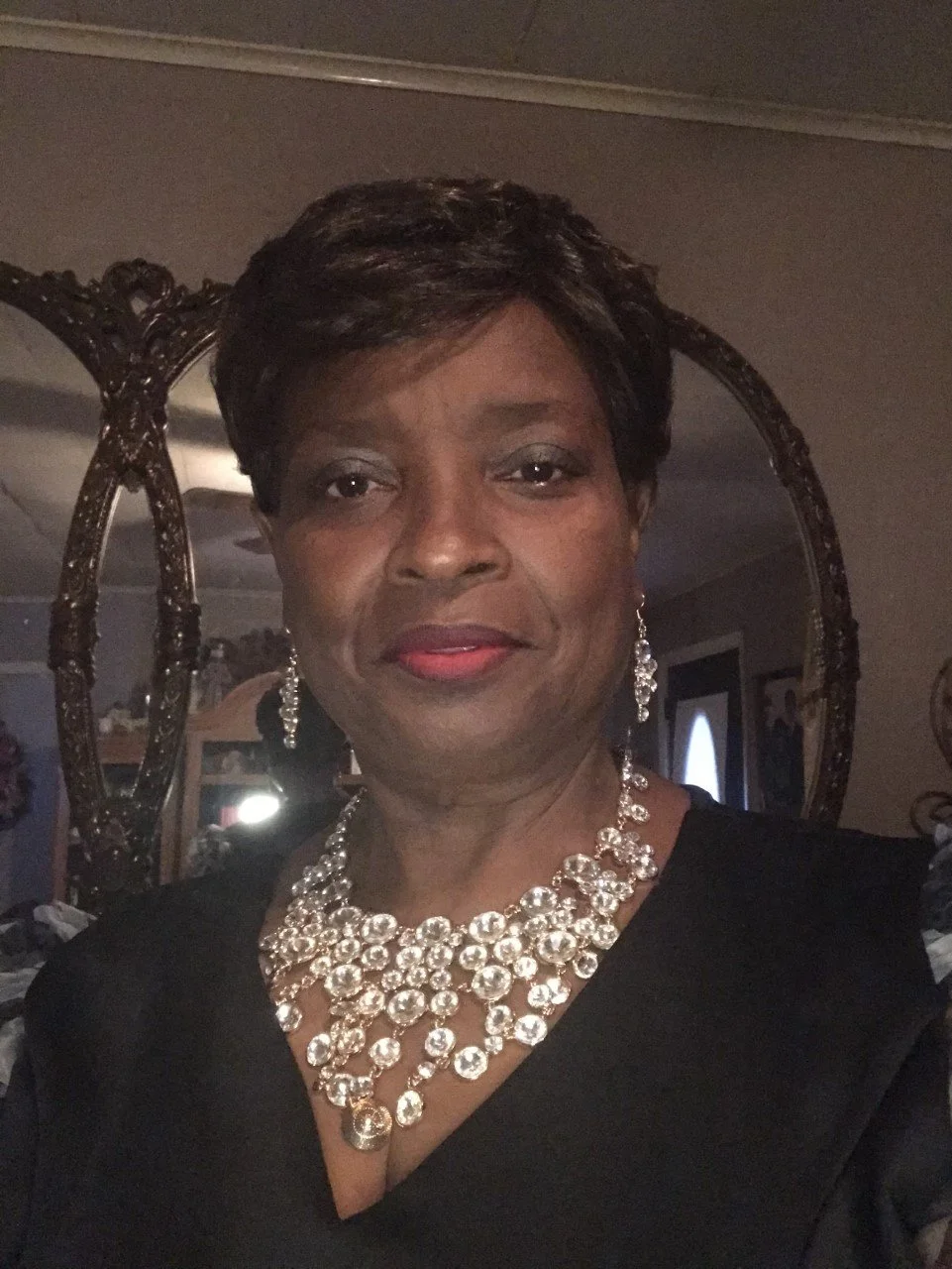Woman wearing a black outfit and a large, sparkling statement necklace in front of a mirror.