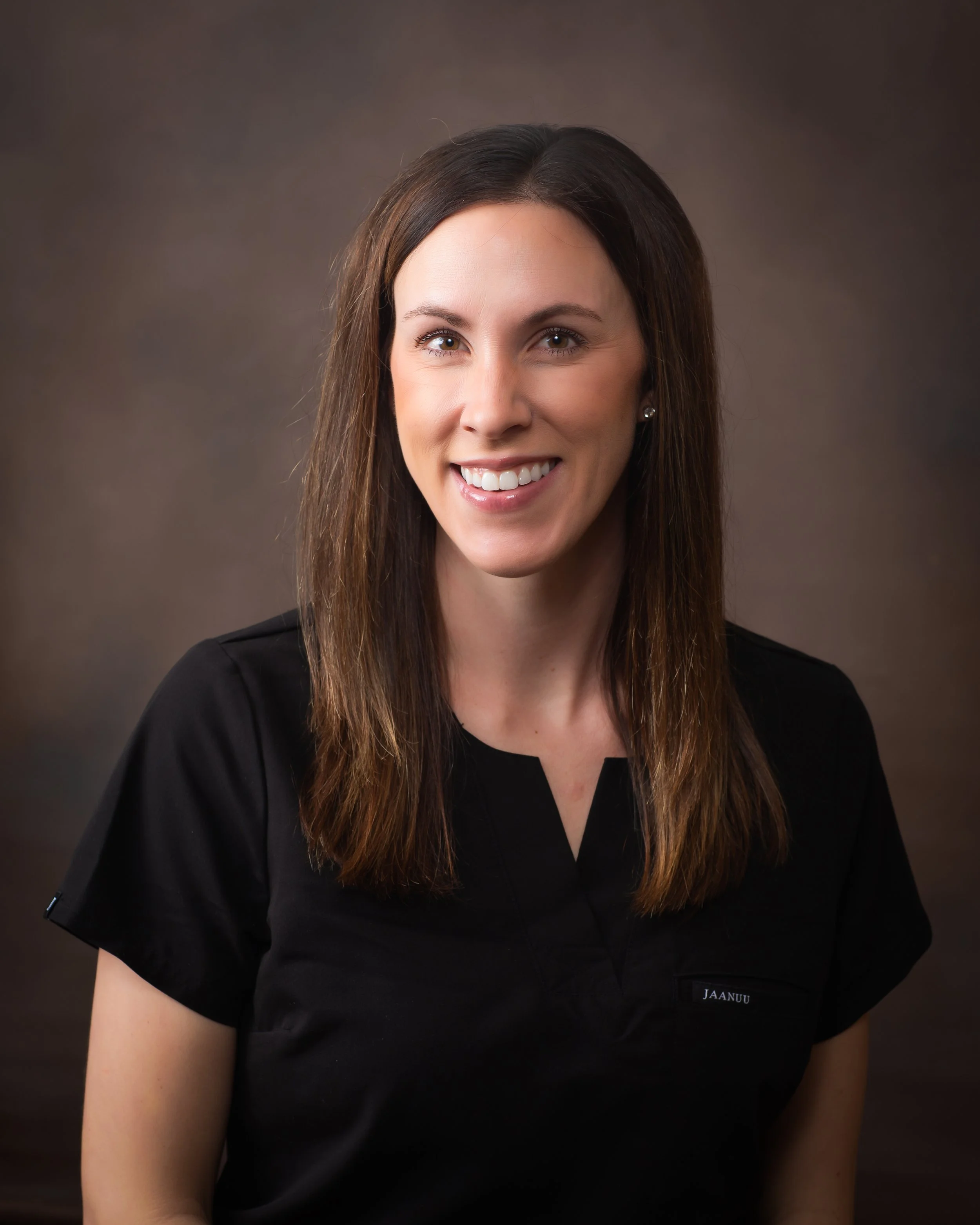 Woman wearing a black shirt, smiling, with long brown hair, against a dark background.