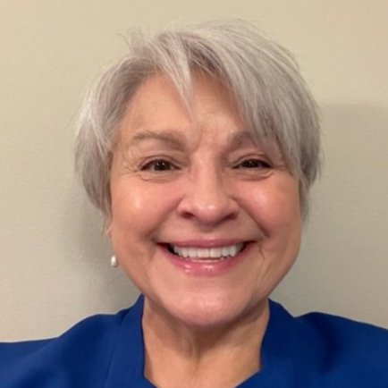 Smiling person with short gray hair wearing a blue shirt against a plain background.