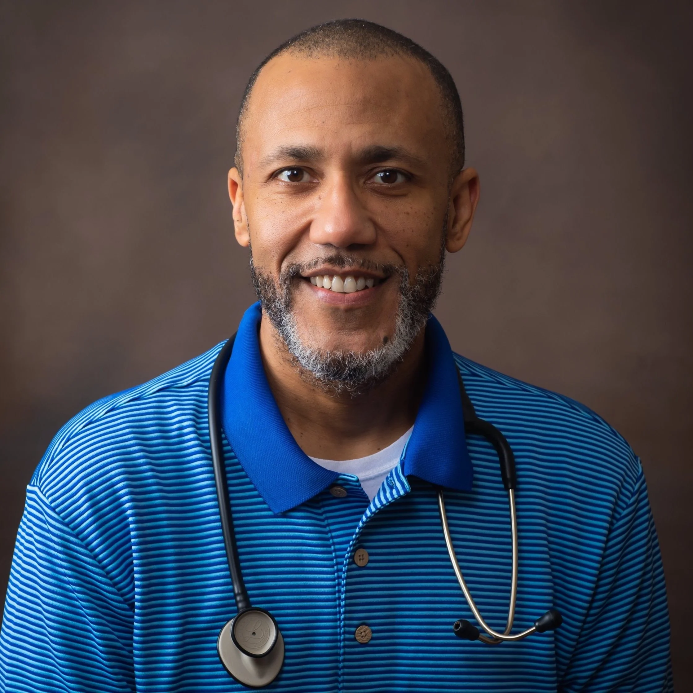 Smiling person wearing a blue striped polo shirt with a stethoscope around their neck, brown background.
