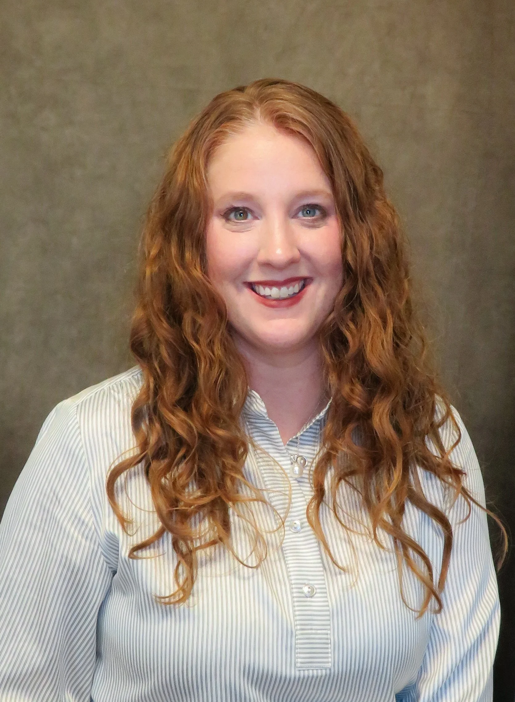 Woman with curly hair smiling in front of a neutral background.