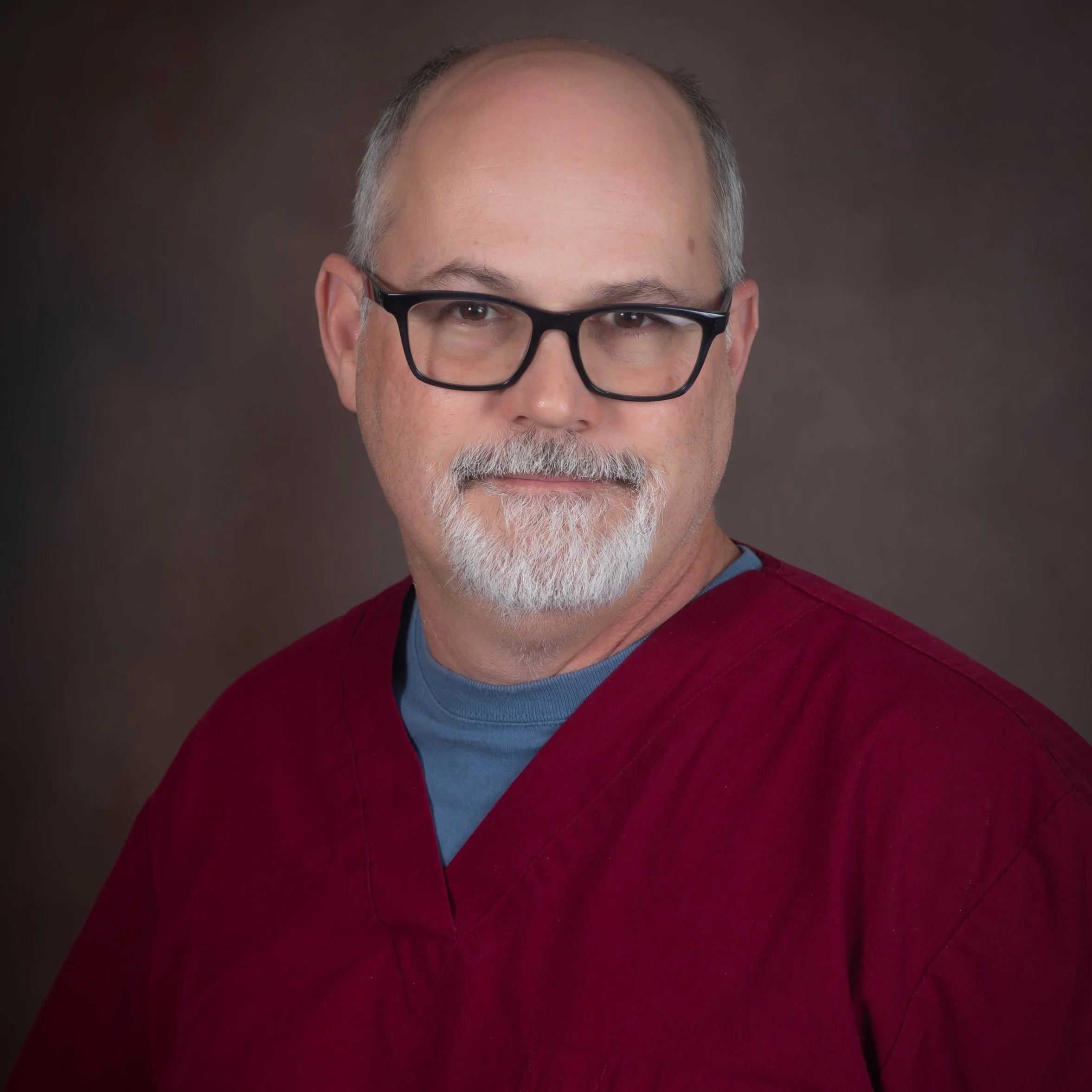 Man wearing glasses and a red shirt with a dark background.