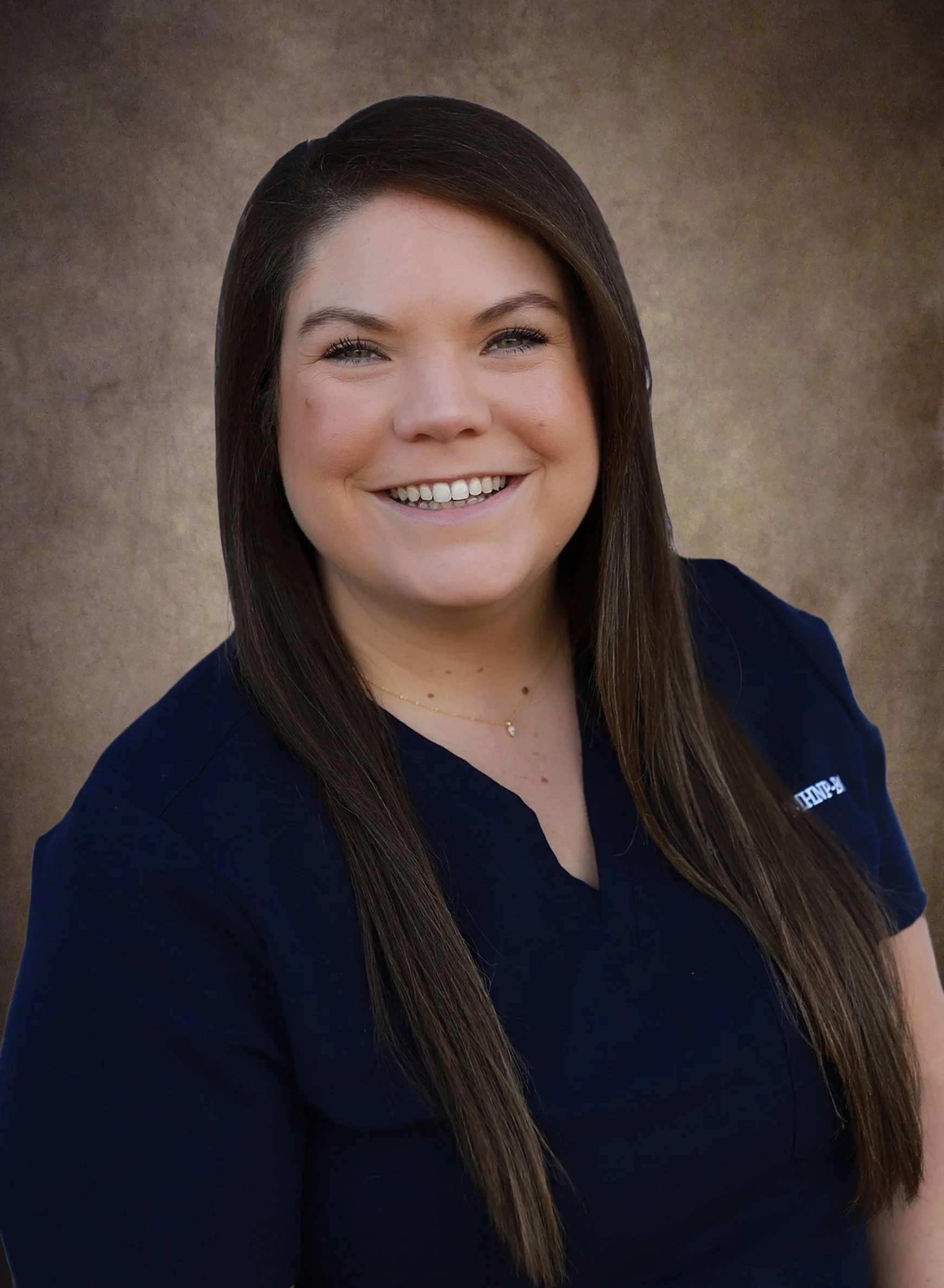 Smiling woman with long brown hair, wearing a dark blue top, against a brown background.