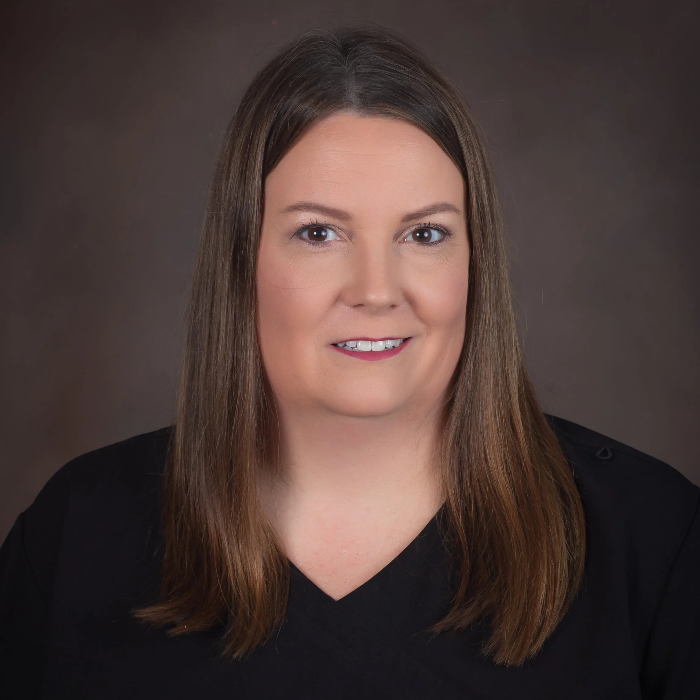 Portrait of a woman with long brown hair and a black top against a dark background.