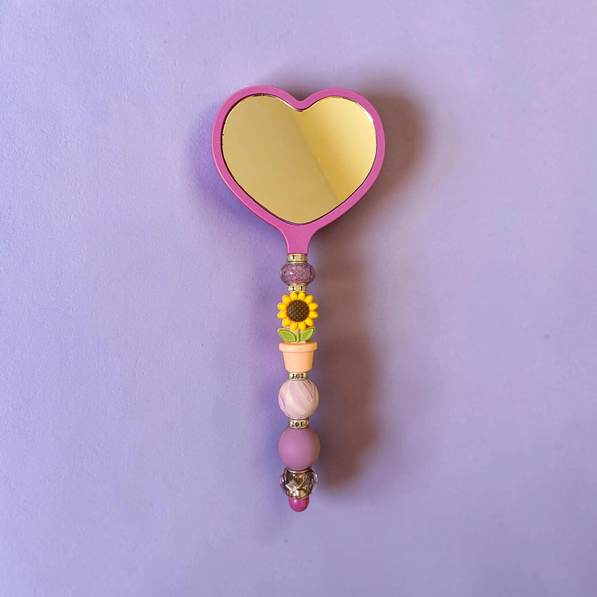 Purple heart shaped mirror with a sunflower in a pot and other rubber beads.