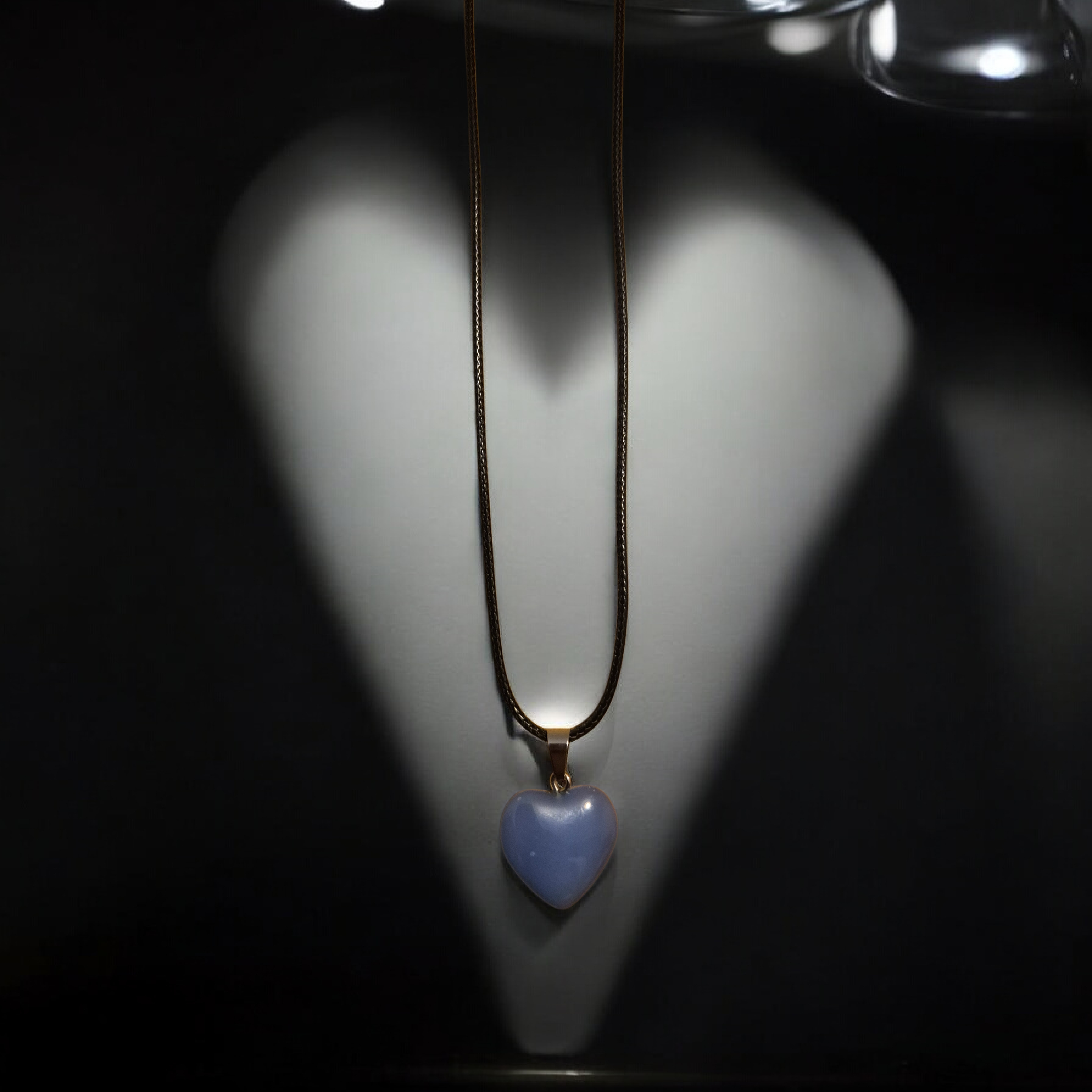 A gold chain necklace with a heart-shaped pendant hanging on a white display bust.