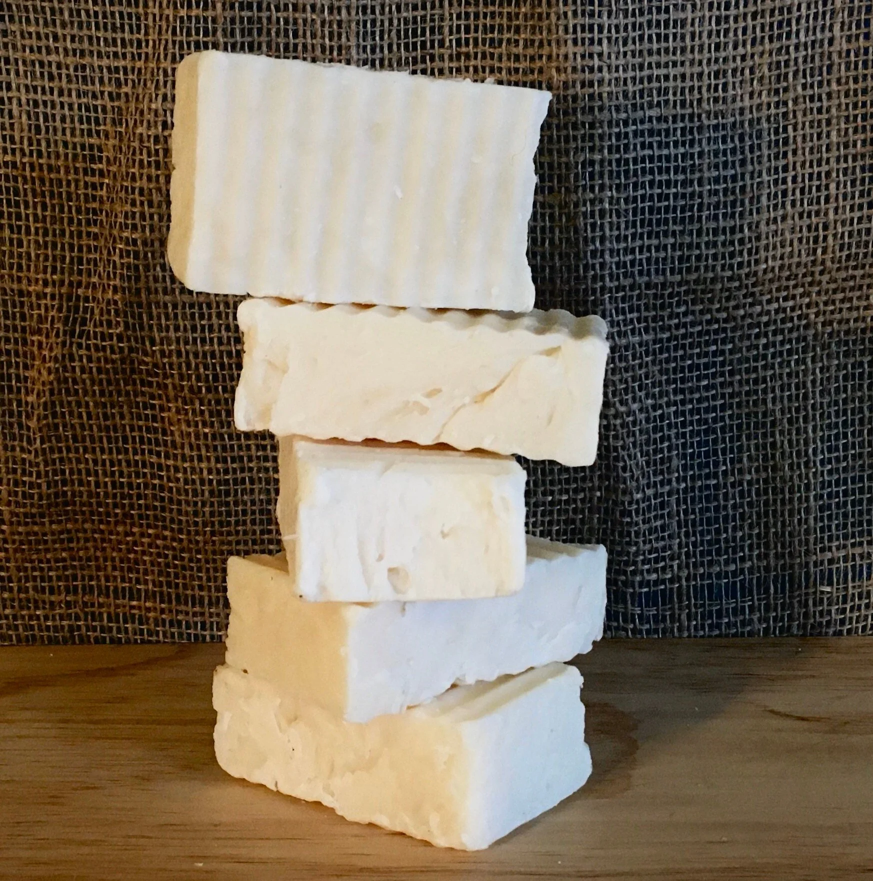 A stack of six white soap bars on a wooden surface with a dark textured background.