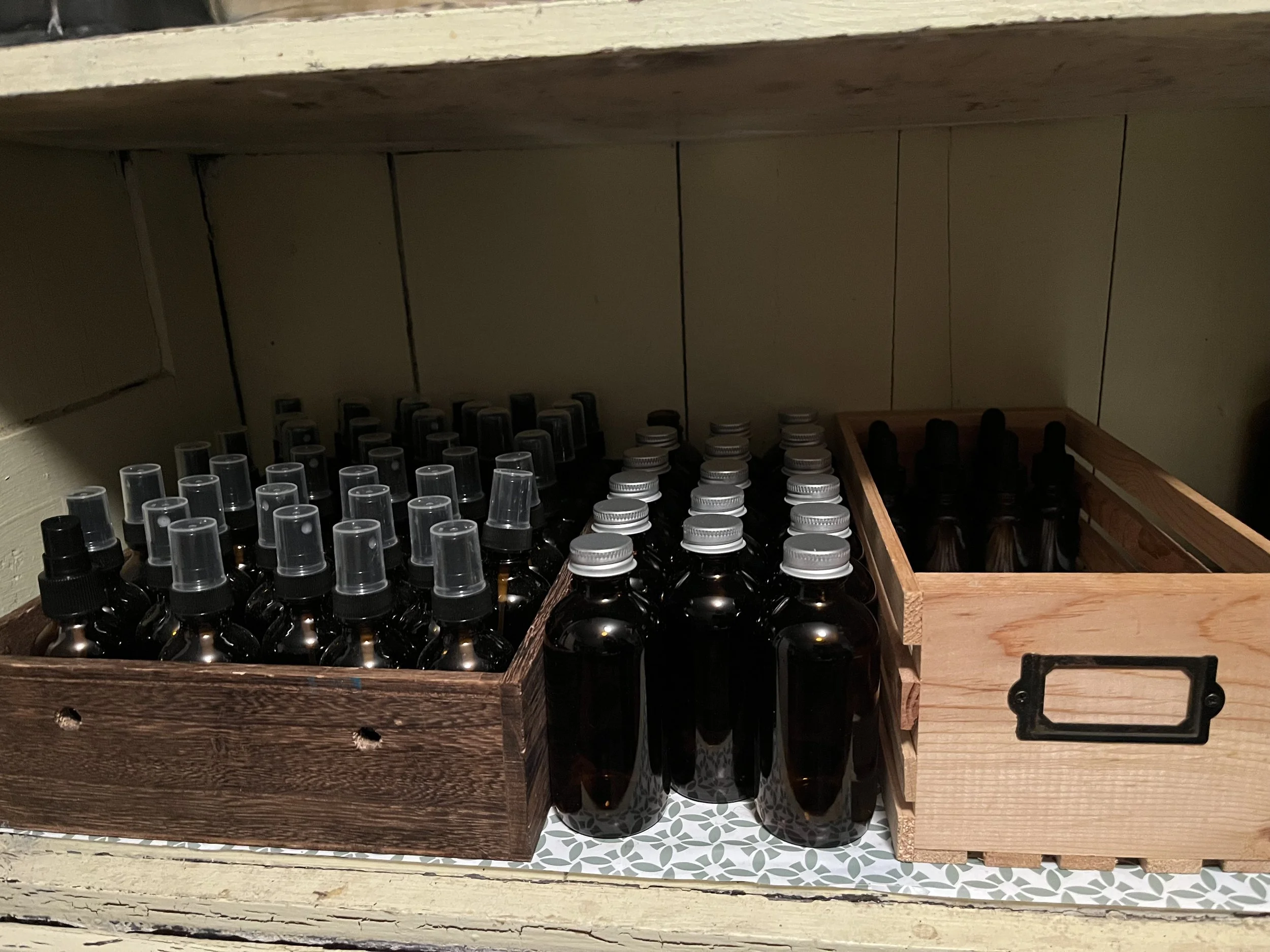 Two wooden storage boxes containing small amber spray bottles and darker bottles with dropper caps, placed on a patterned surface inside a cabinet.
