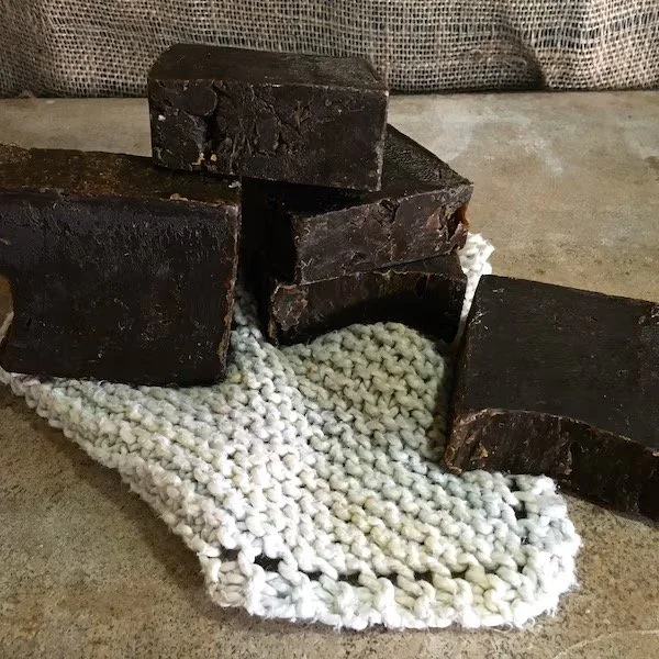Several dark-colored soap bars stacked on a textured white cloth on a beige surface.