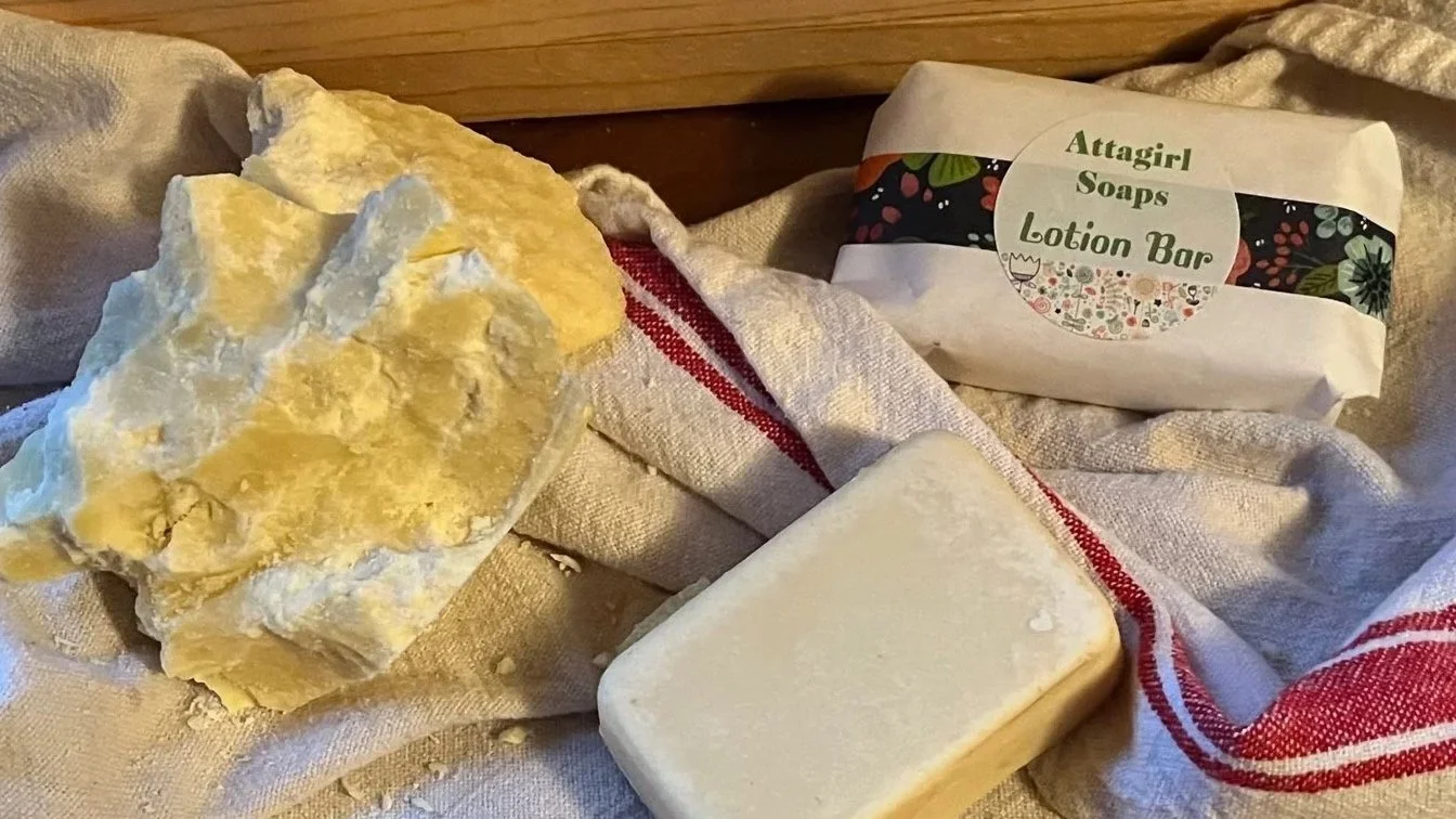 A large soapstone block, a bar of soap, and a wrapped lotion bar on a white cloth with red stripes.