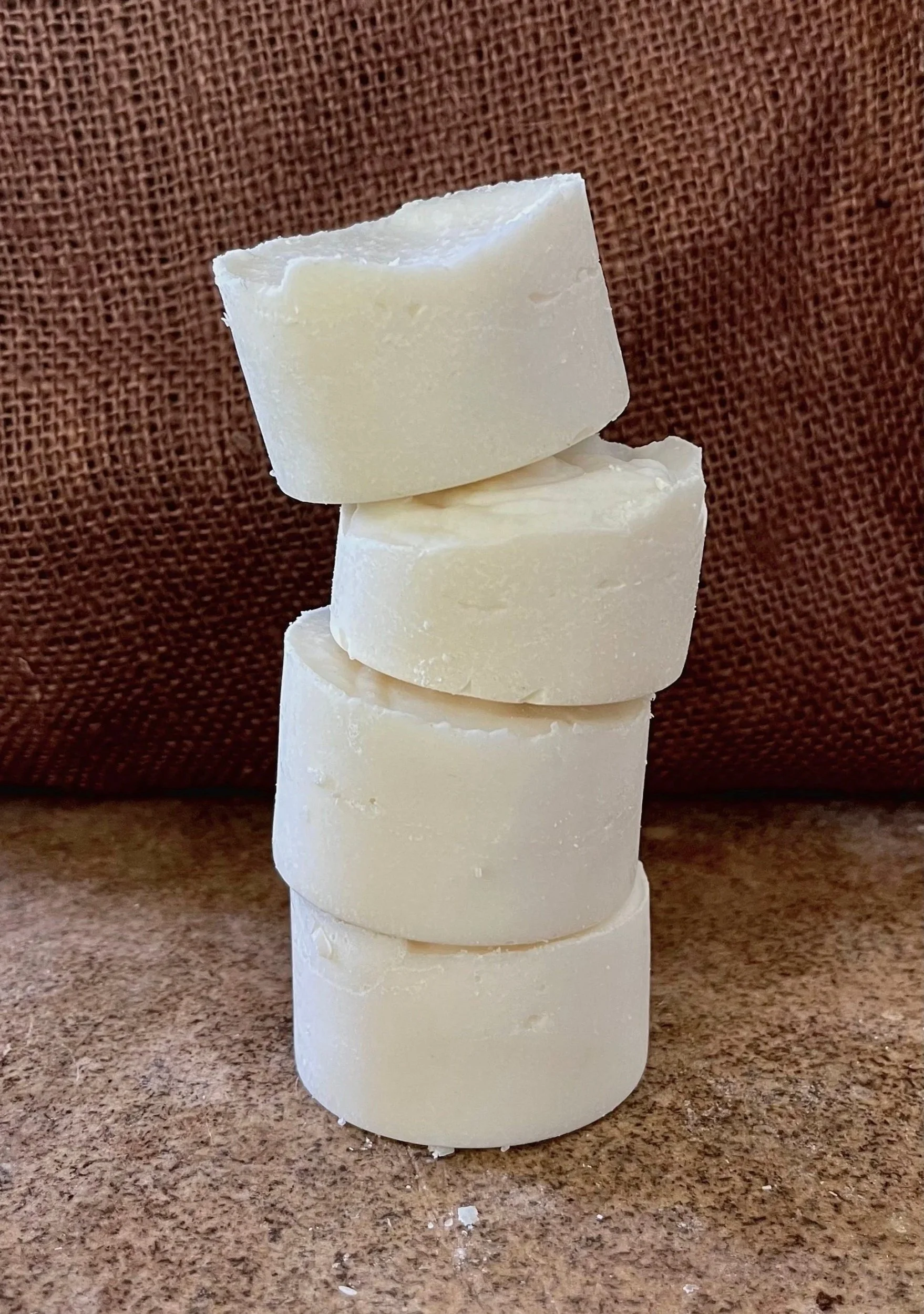 Four cylindrical white soap bars stacked on top of each other with a textured brown background.