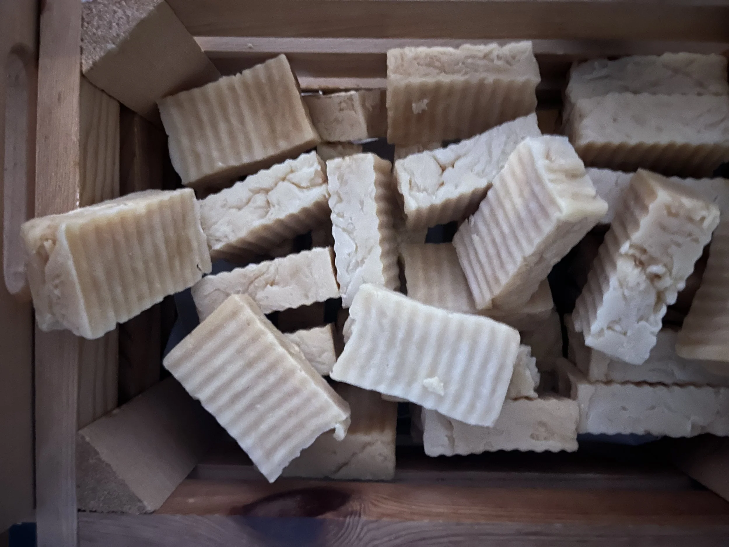 Various bars of soap with some having ridged surfaces and others with rough, uneven textures in a wooden basket.