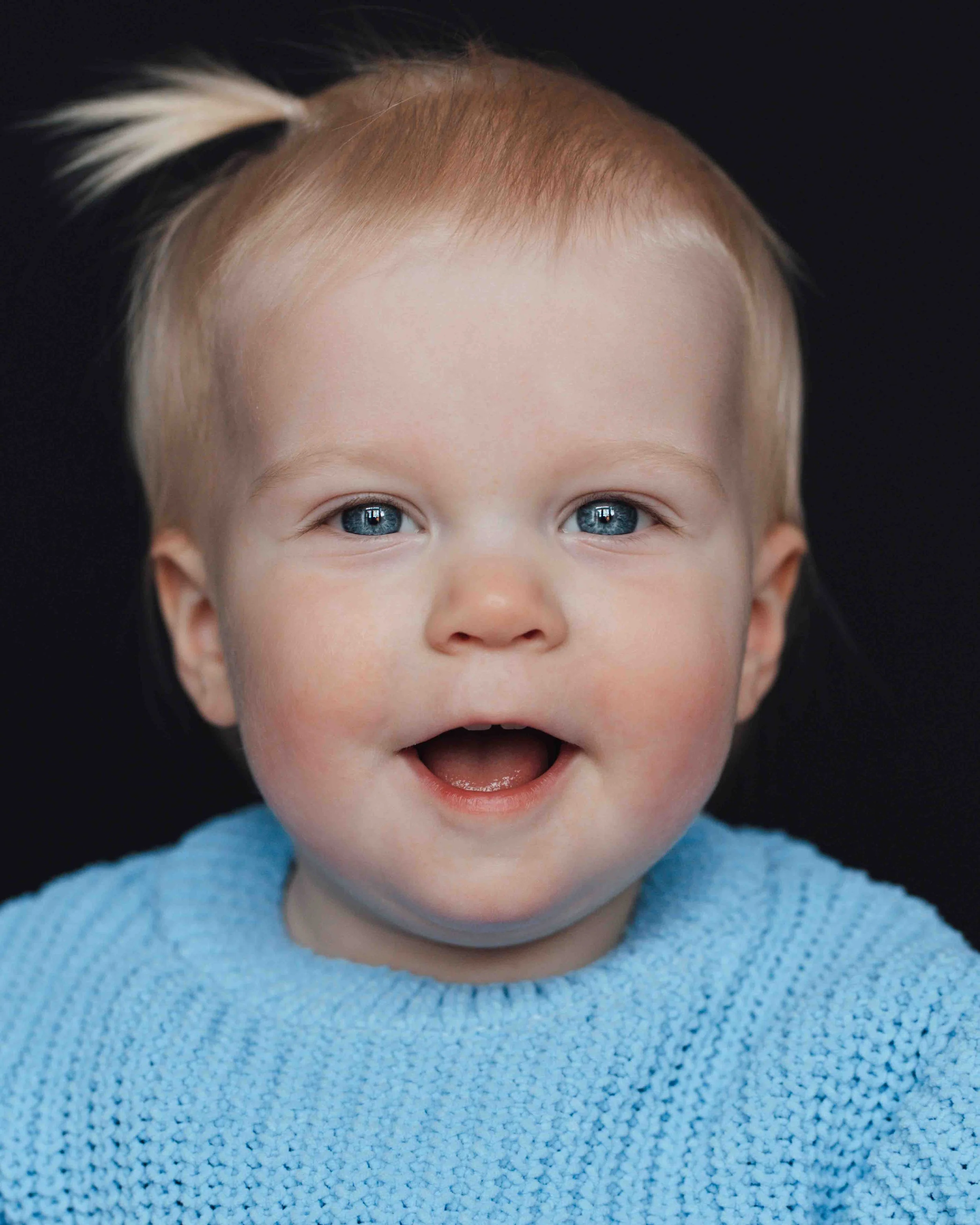 Kinderportret van een schattig meisje van 1 jaar met blauwe ogen en een zwarte achtergrond