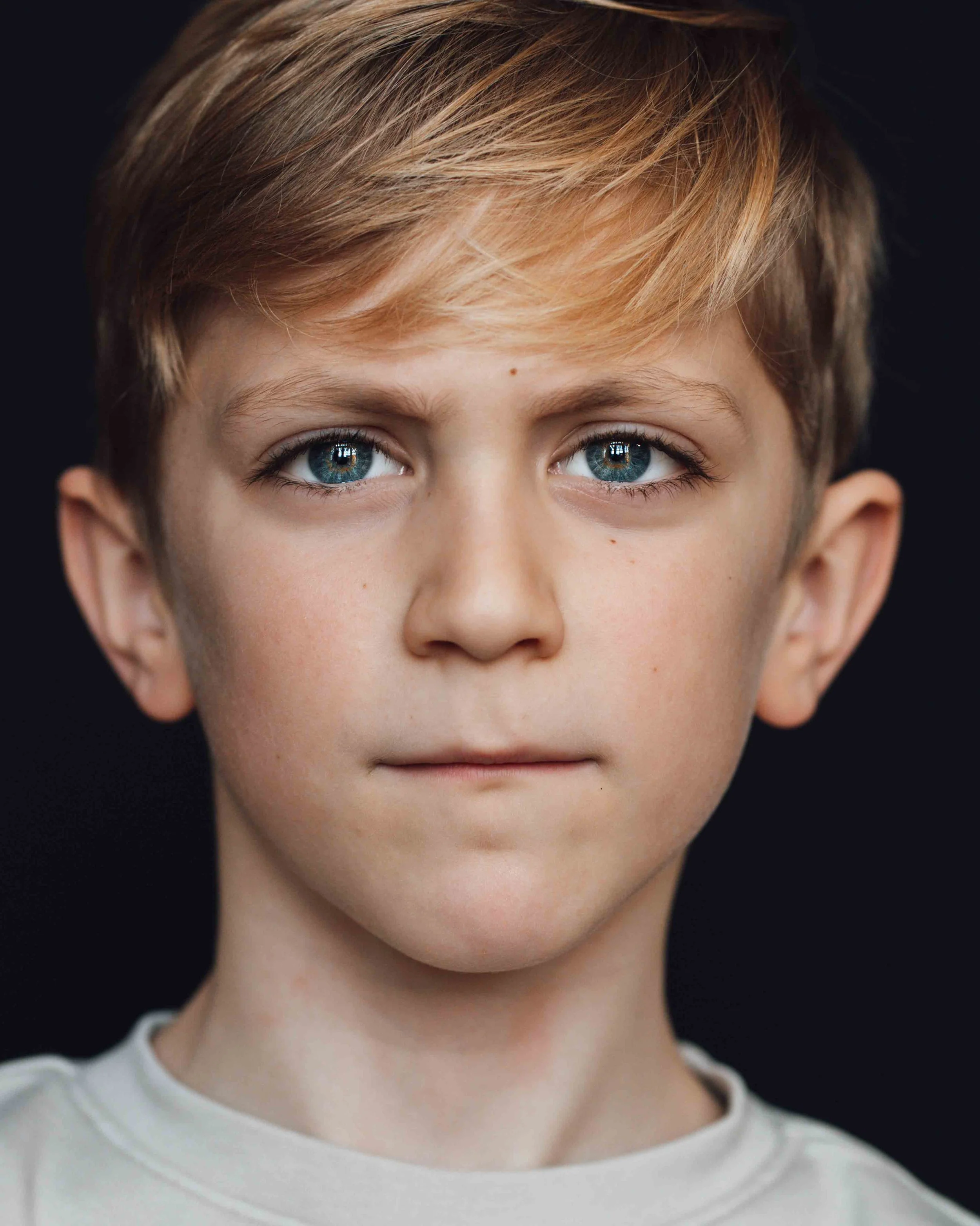 Portret van een jongen van 7 jaar met blauwe ogen en zwarte achtergrond
