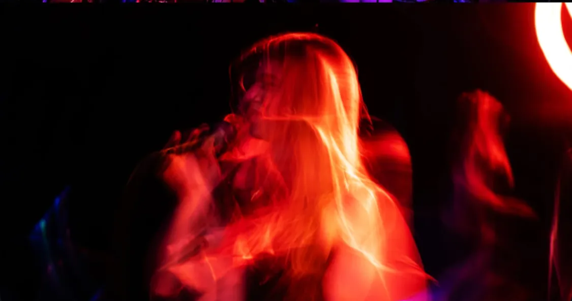Blurry red and orange neon lights creating an abstract image of two people in a dark environment.