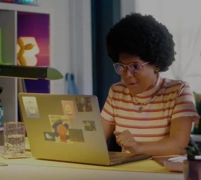 Person with curly hair and glasses working on a laptop at a desk.