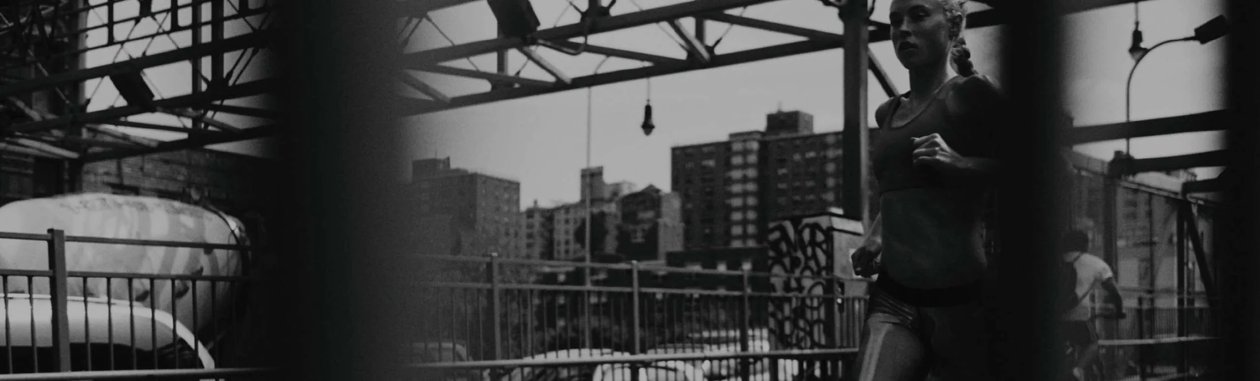 A woman running on an urban rooftop with city buildings in the background, captured in black and white.