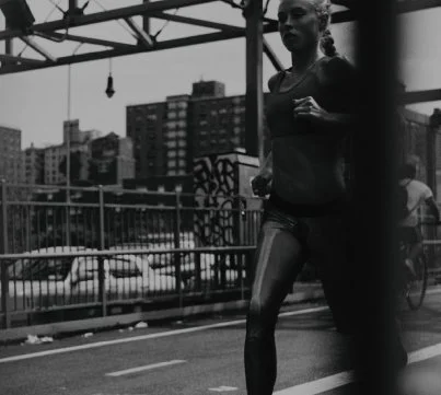 A woman jogging on a city street at night with city buildings in the background.