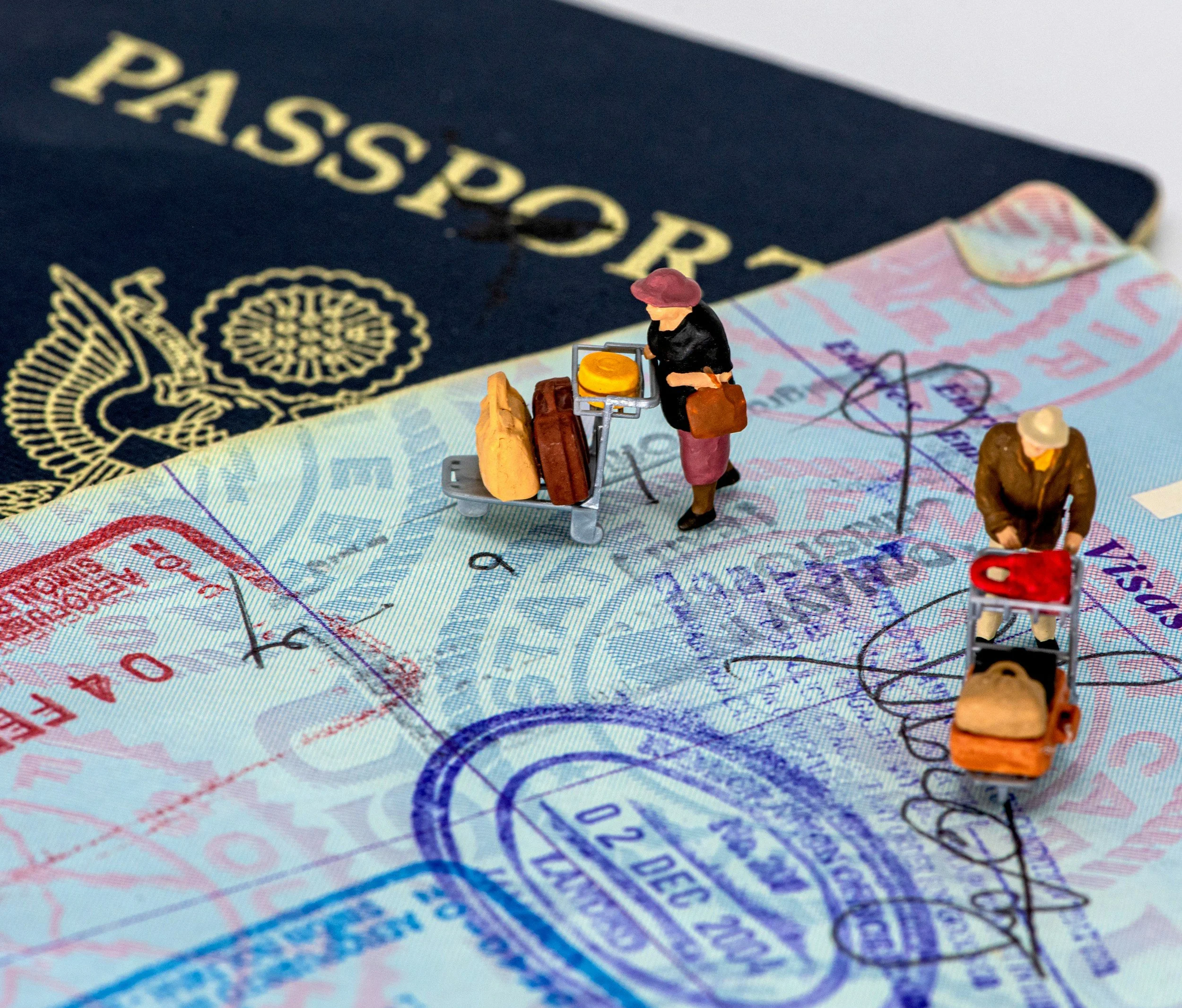 Miniature figurines of travelers with carts placed on a passport and travel documents.
