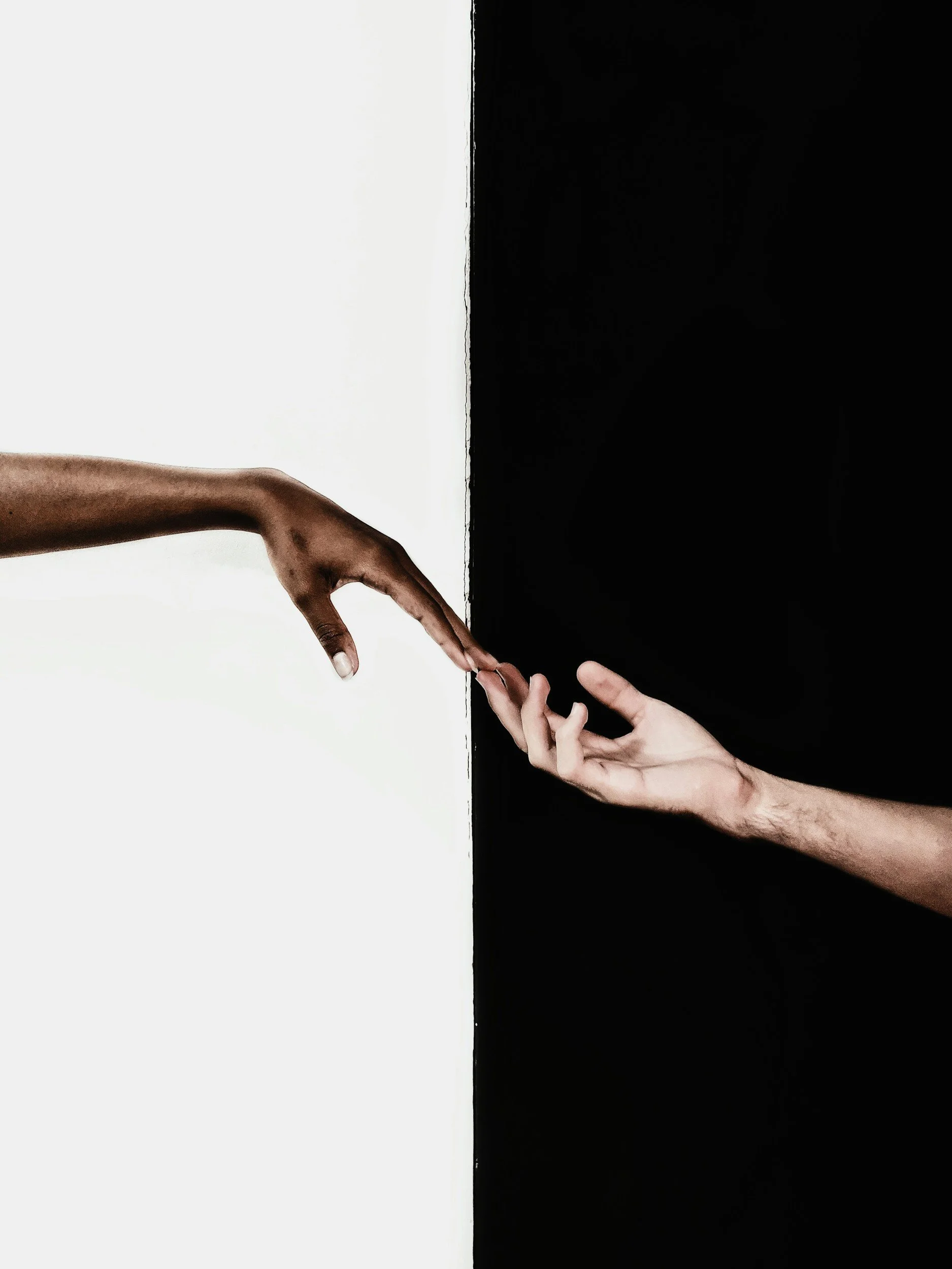Two hands reaching towards each other, one on the left side of the image and one on the right, with a contrasting black and white background.