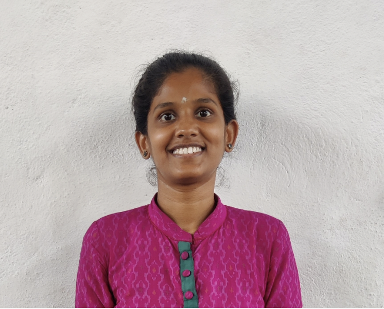 A young woman with dark hair tied back, wearing a vibrant pink traditional outfit, smiling against a plain white wall.