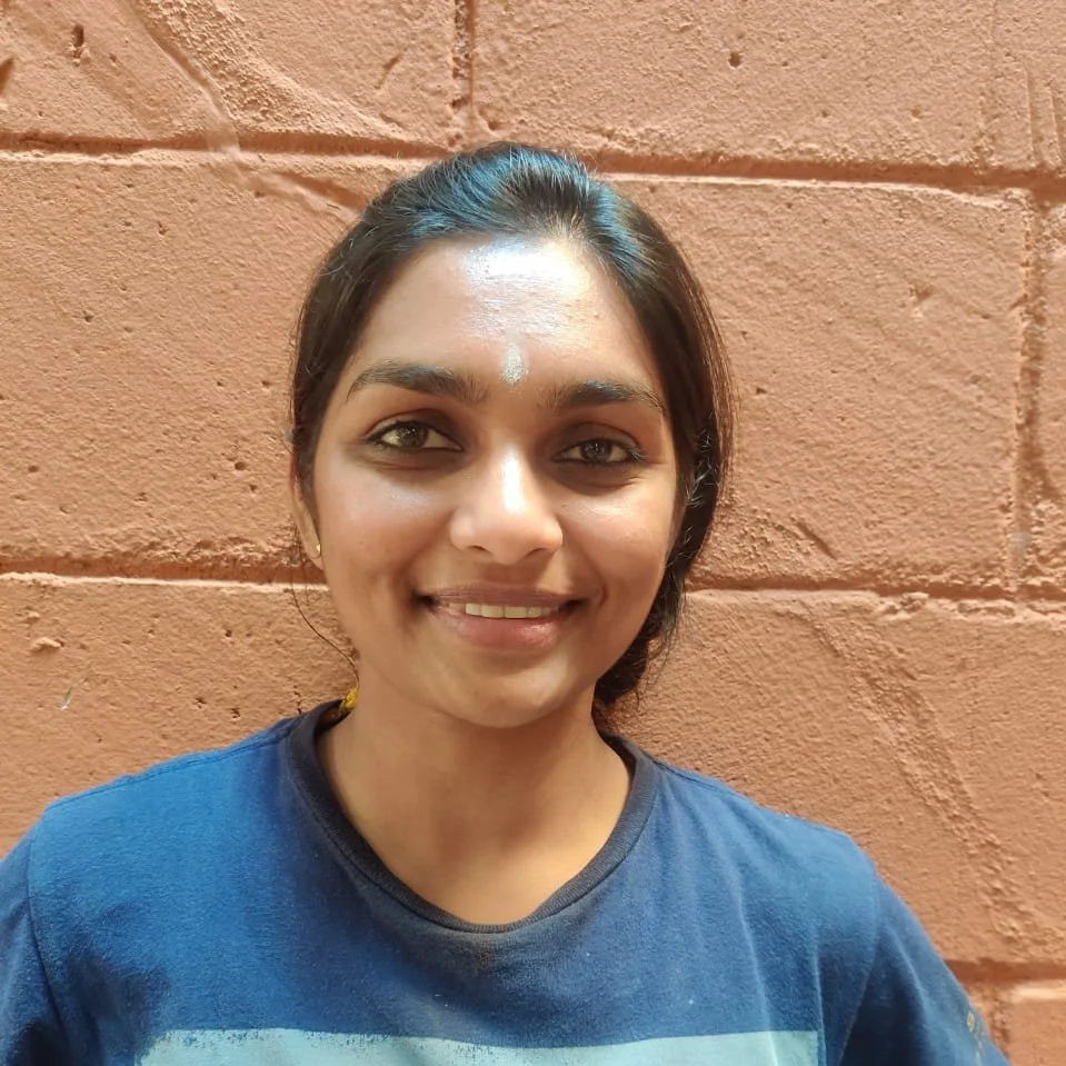 A woman smiling with a painted mark on her forehead, standing in front of a brick wall.