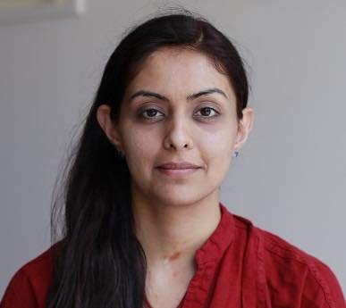 A woman with long dark hair, wearing a red top, looking at the camera with a neutral expression.