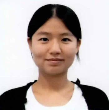 A woman with black hair, wearing a black jacket over a white shirt, looking at the camera against a plain white background.