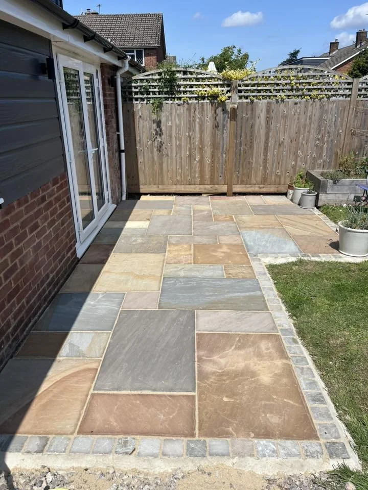 Backyard patio with multi-colored slate tiles, a wooden privacy fence, and potted plants with a garden bed.