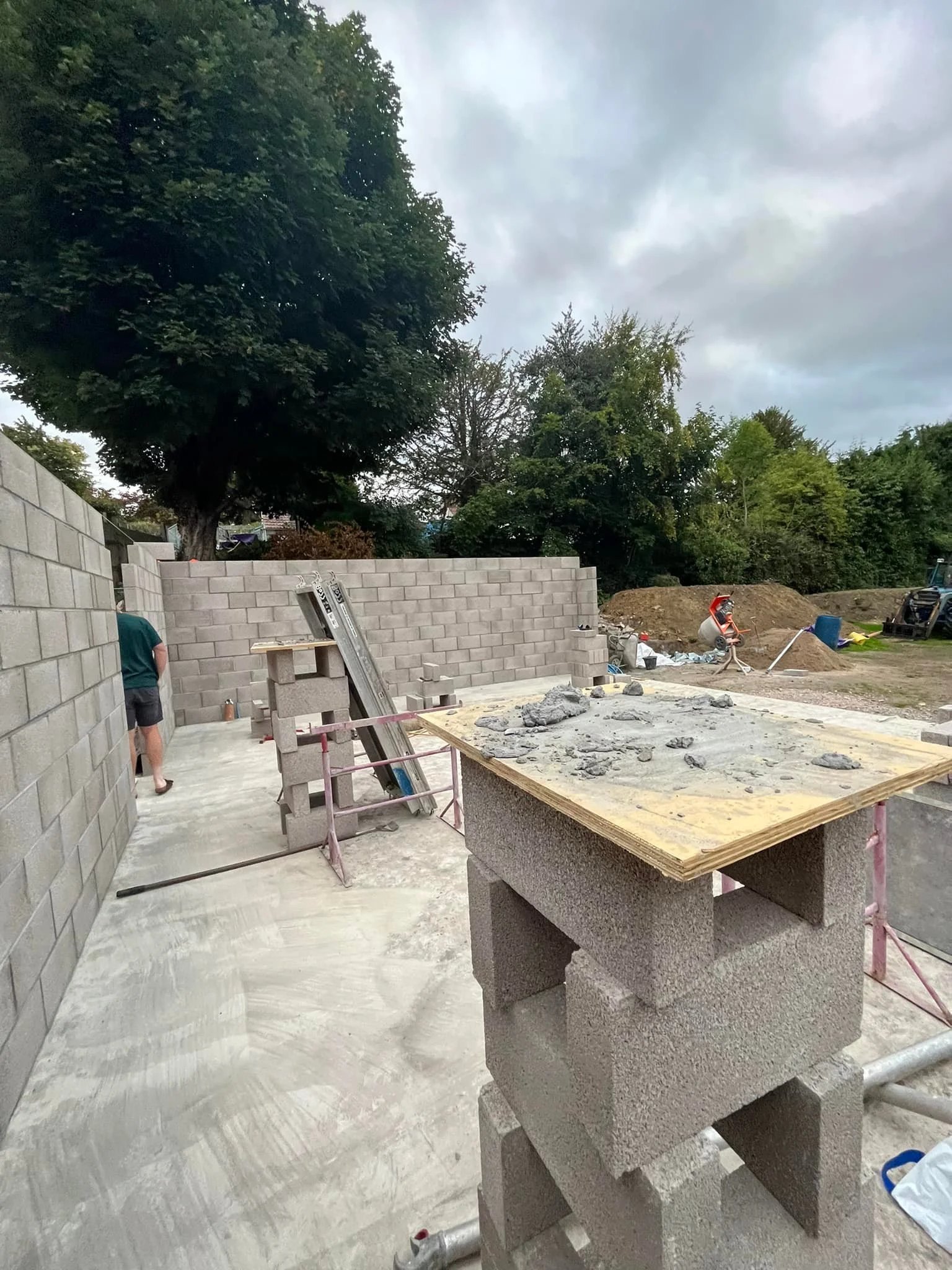 Construction site with concrete blocks, work table, and workers building a wall outdoors under cloudy skies