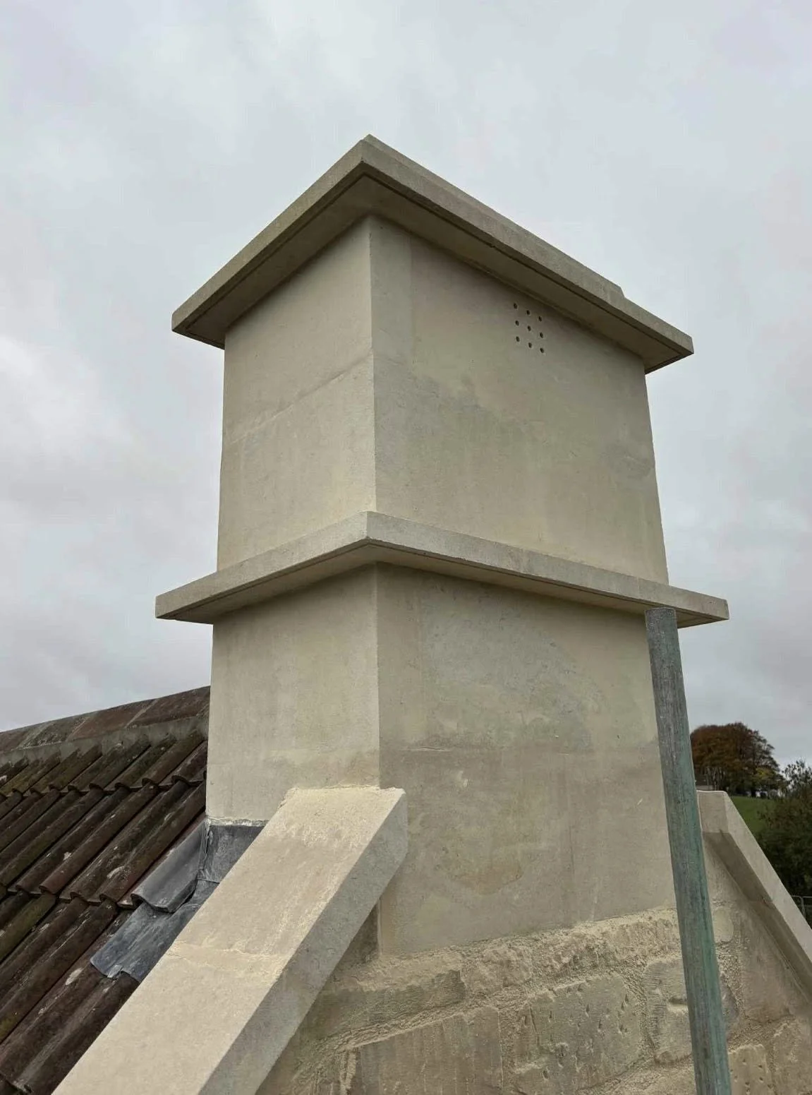 Close-up of a chimney on a roof with a cloudy sky in the background.
